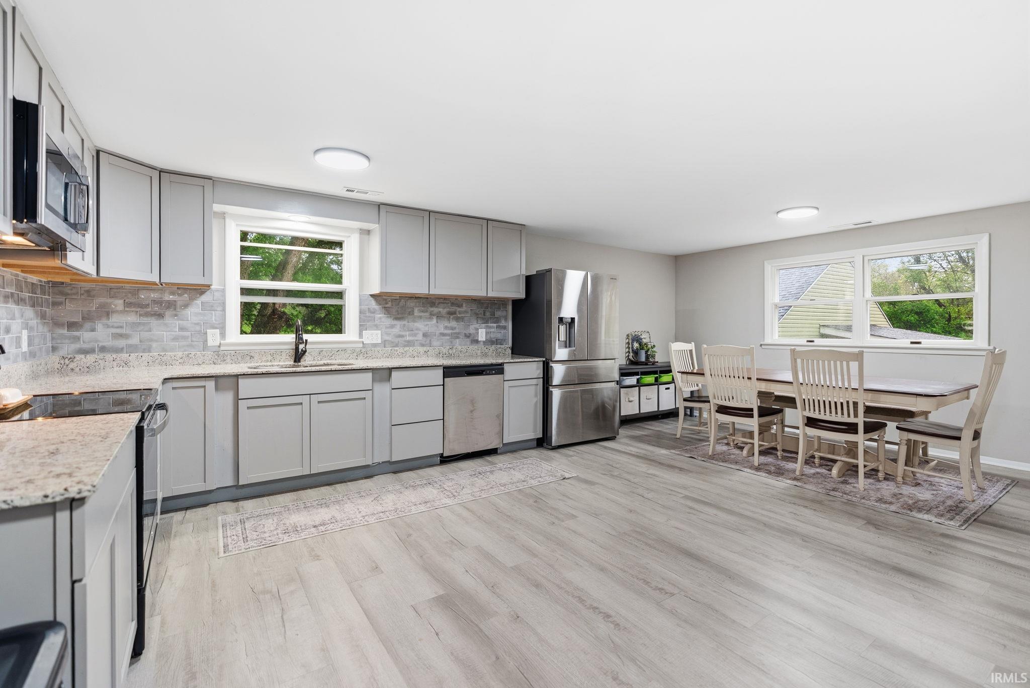 Spacious kitchen and dining area featuring light gray cabinetry, stainless steel appliances, granite countertops, and a subway tile backsplash