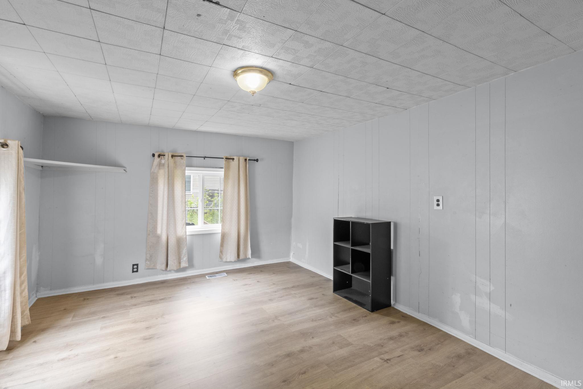 Room featuring wood-finish flooring, light grey paneled walls, and a white framed window