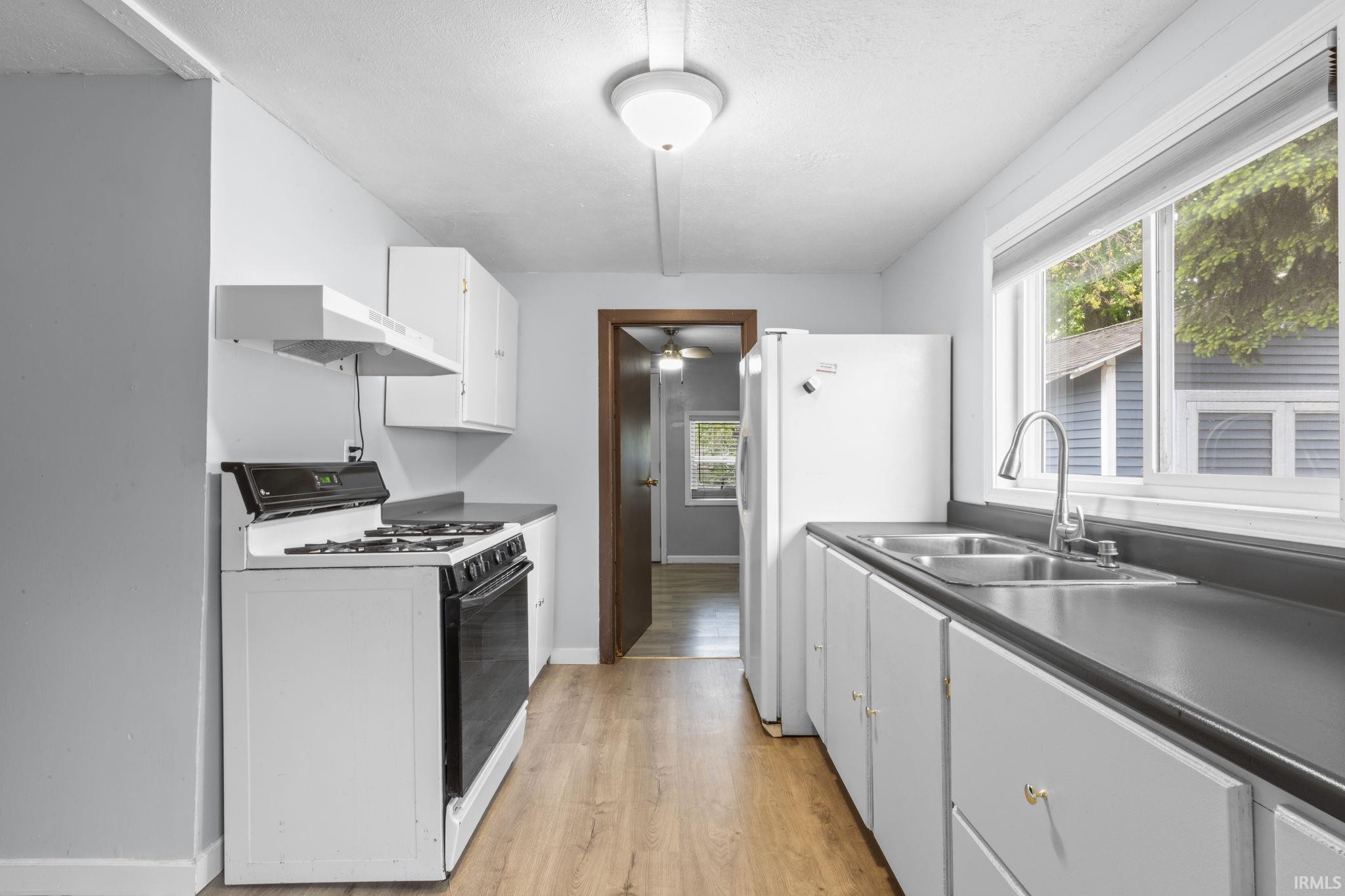 Kitchen featuring wood-finish flooring, white cabinetry, dark countertops, and a double basin stainless steel sink with a gooseneck faucet