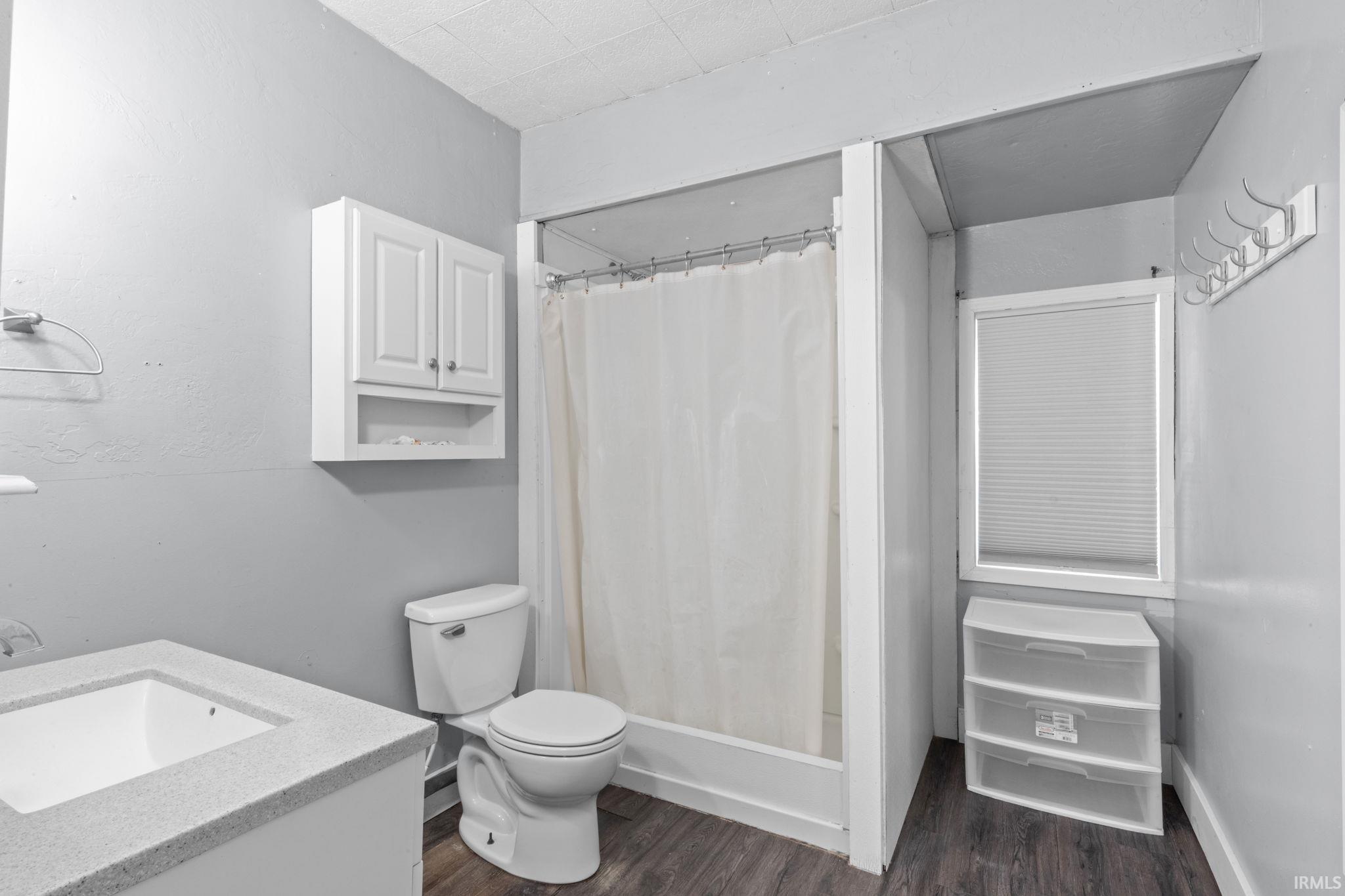 Bathroom featuring a vanity with an integrated sink, a toilet, and a shower/tub combination with a white curtain