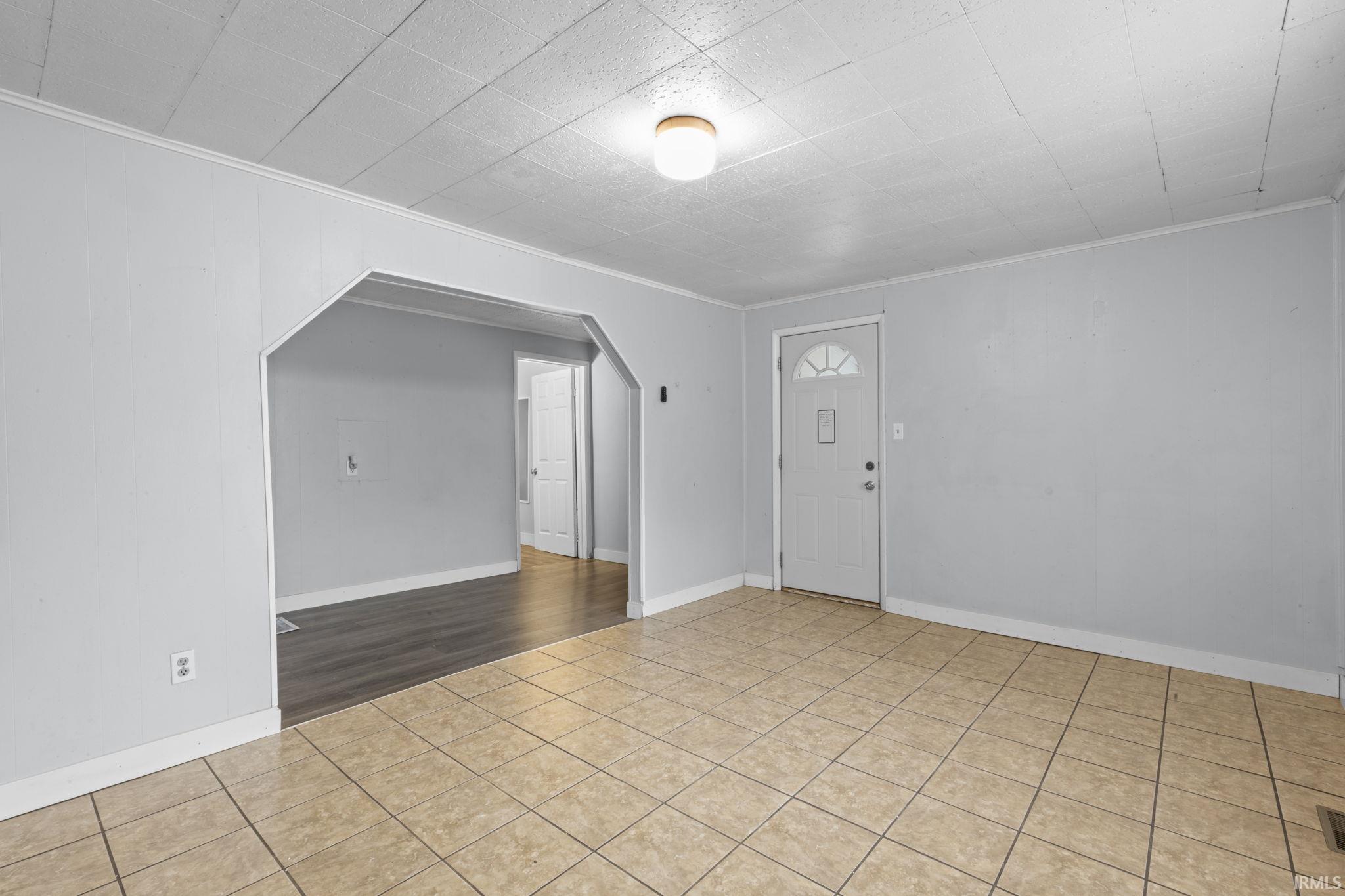 Entry area with neutral tile flooring, white trim, and a decorative archway