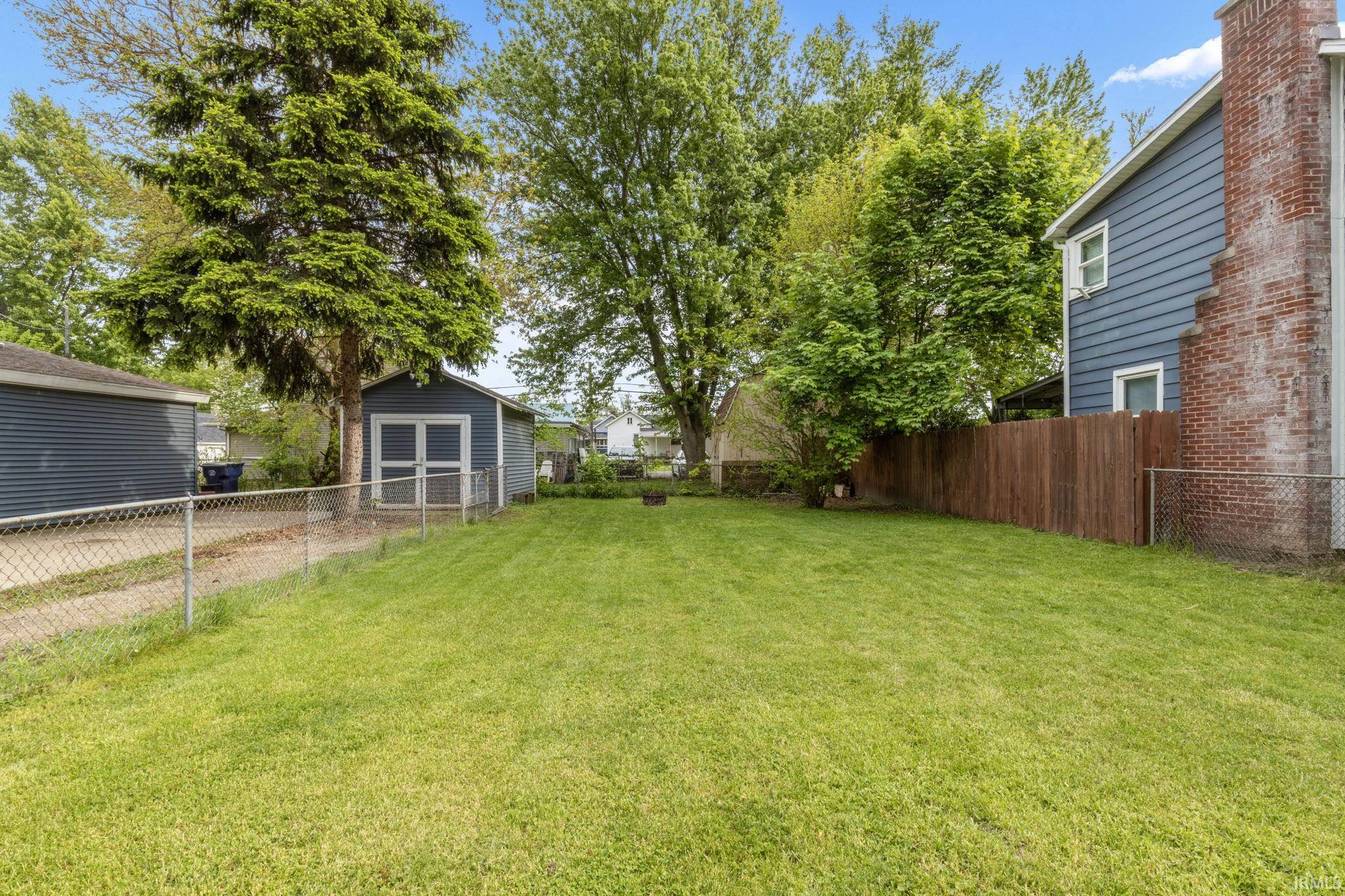 Generous backyard featuring a manicured lawn, established trees, a storage shed, and a privacy fence
