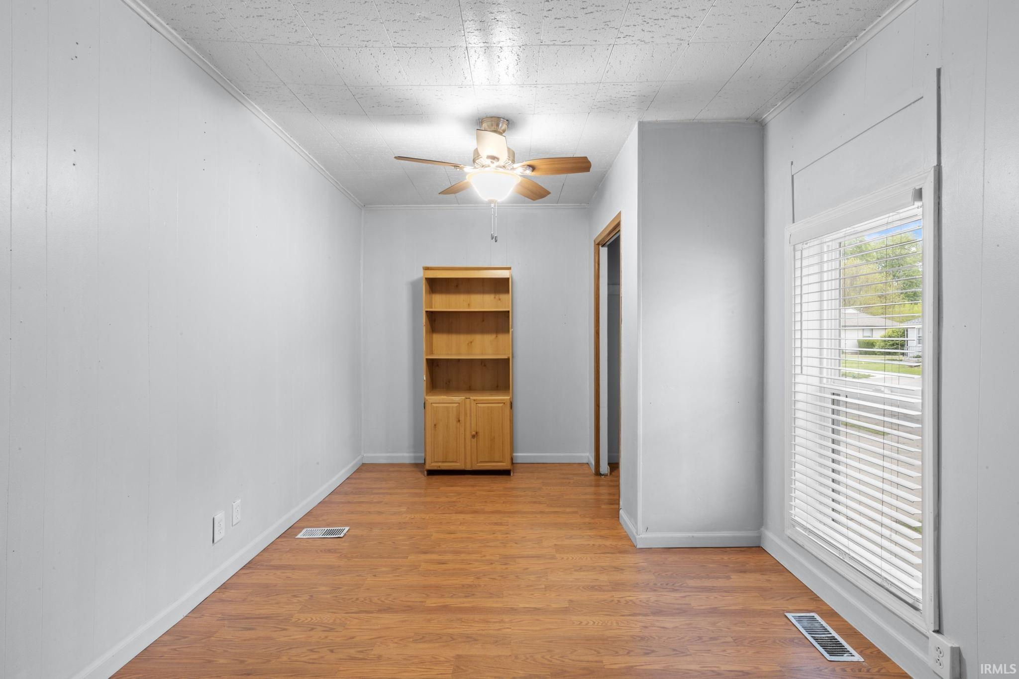 Room with light wood-finish flooring, white paneling, and a white ceiling with crown molding