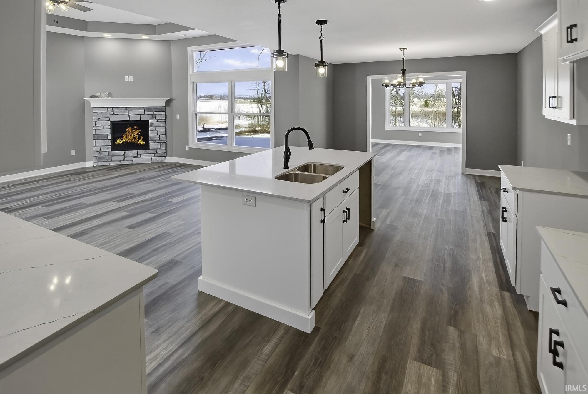 Kitchen with a stone fireplace, open floor plan, white cabinets, dark wood-style flooring, and a kitchen island with sink