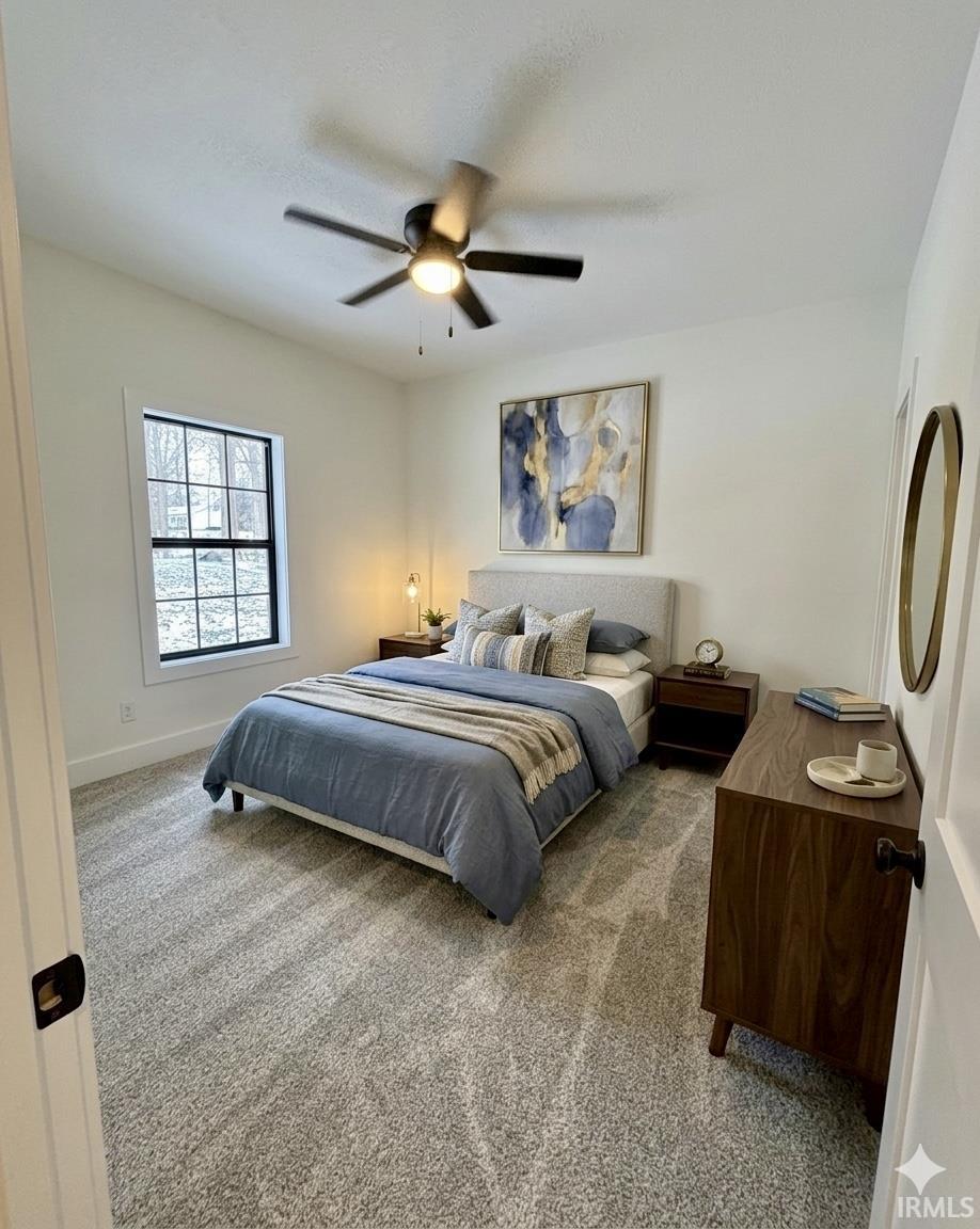 Bedroom featuring neutral-toned carpeting, a multi-pane window with dark trim, a ceiling fan with integrated lighting, and white baseboards