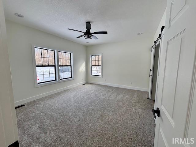 Spacious room featuring light-colored carpeting, multiple windows with black framing, a black ceiling fan, recessed lighting, and a white barn door with black hardware
