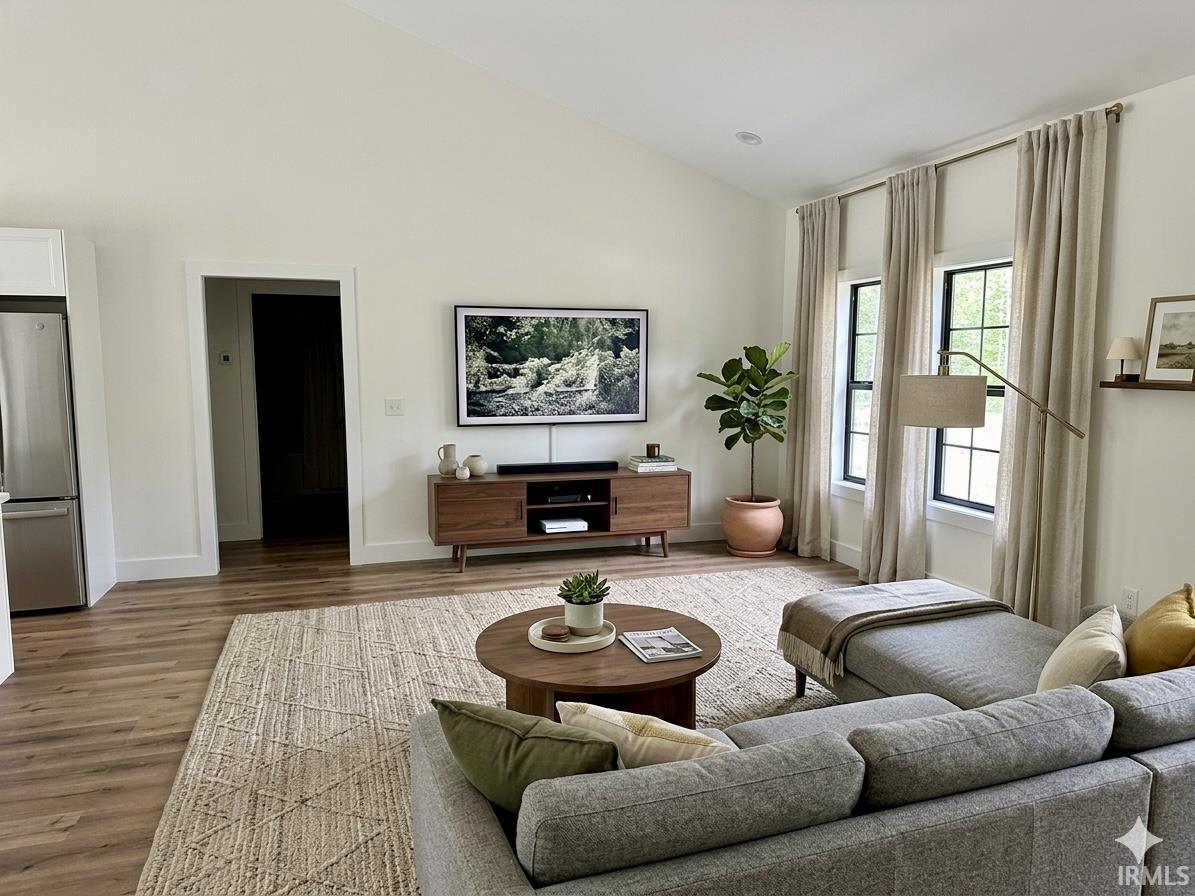 Vaulted living room featuring wood-finish flooring, white painted walls, and black-framed windows with light-colored drapery