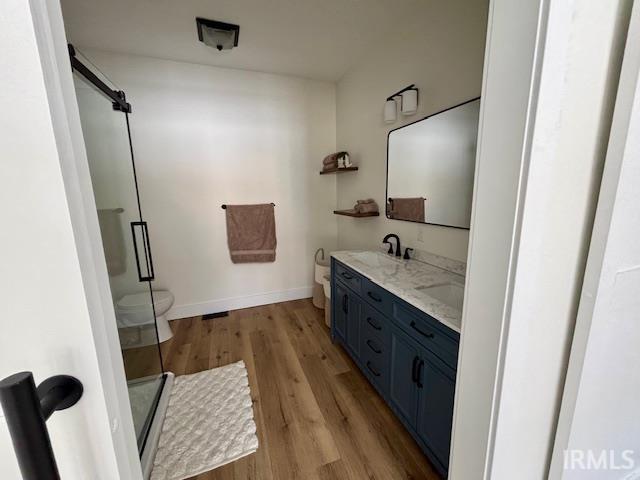 Bathroom featuring wood-finish flooring, a frameless glass shower enclosure with a sliding barn door, a dual-sink vanity with a light-colored countertop and dark blue cabinetry, and a black-framed rectangular mirror
