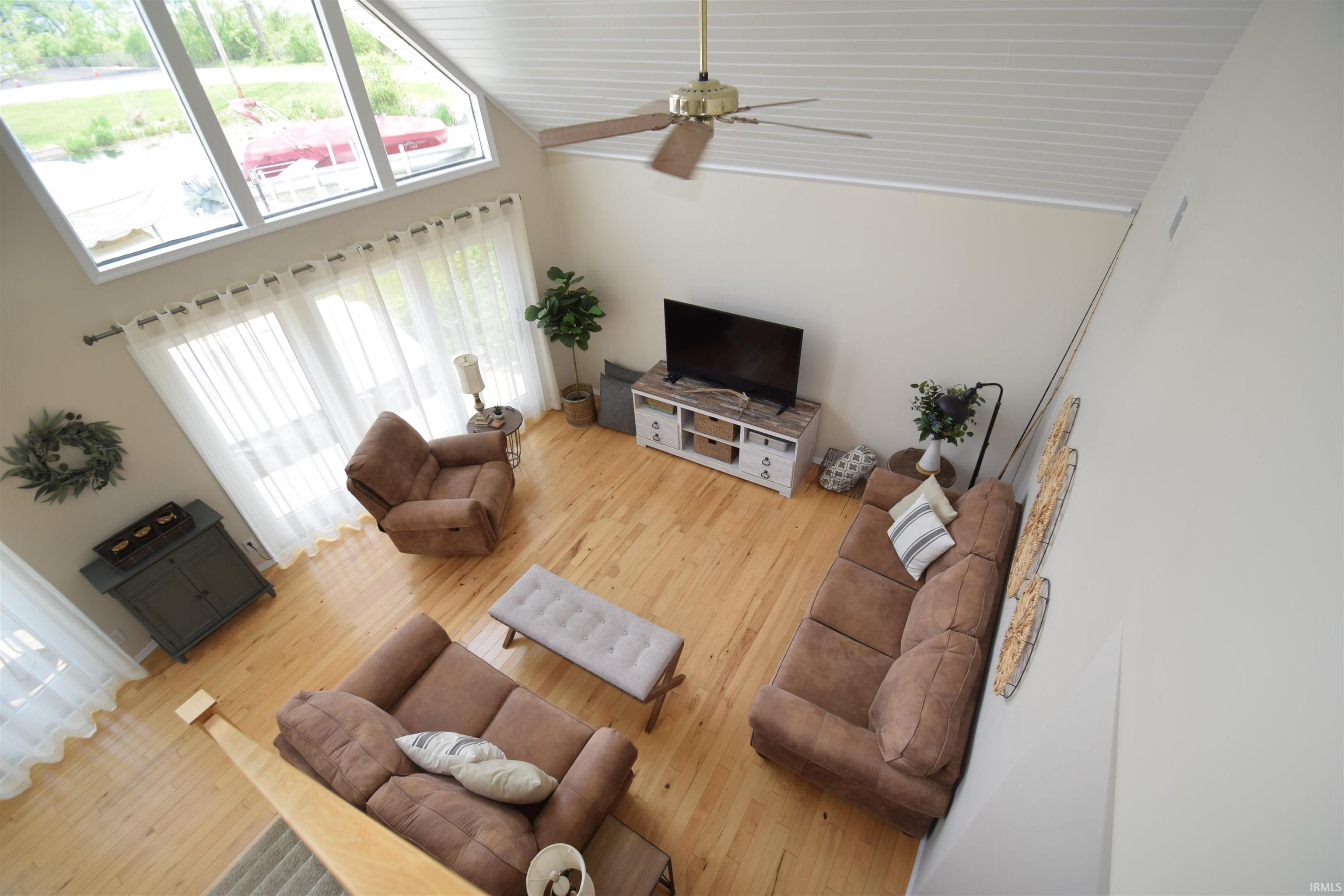 Vaulted ceilings with a ceiling fan, light wood-finish flooring, and expansive windows