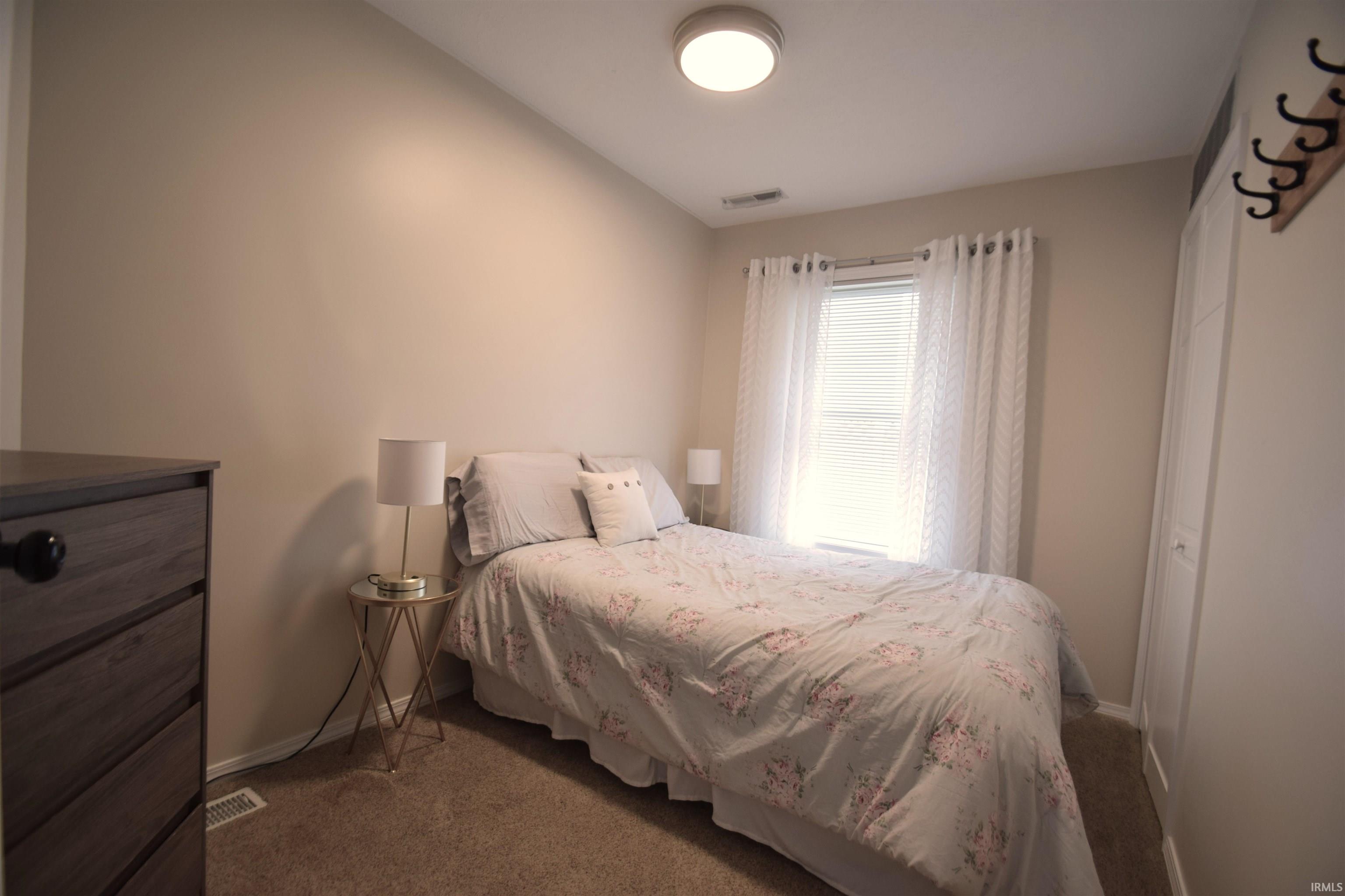Carpeted bedroom featuring a flush-mount ceiling light, a window with blinds and sheer curtains, and a built-in closet with a white door