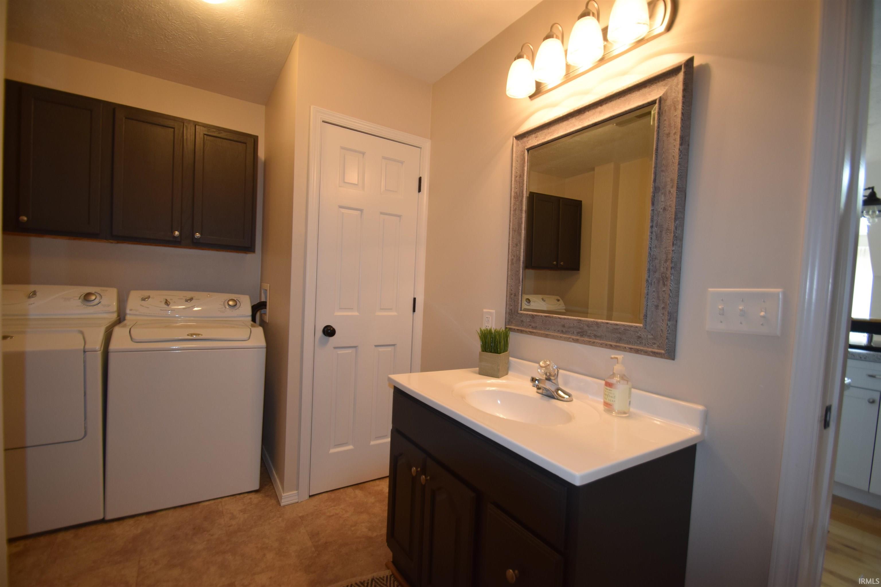 Utility area featuring a dark wood-finish vanity with a white countertop and basin sink, framed mirror, and overhead lighting