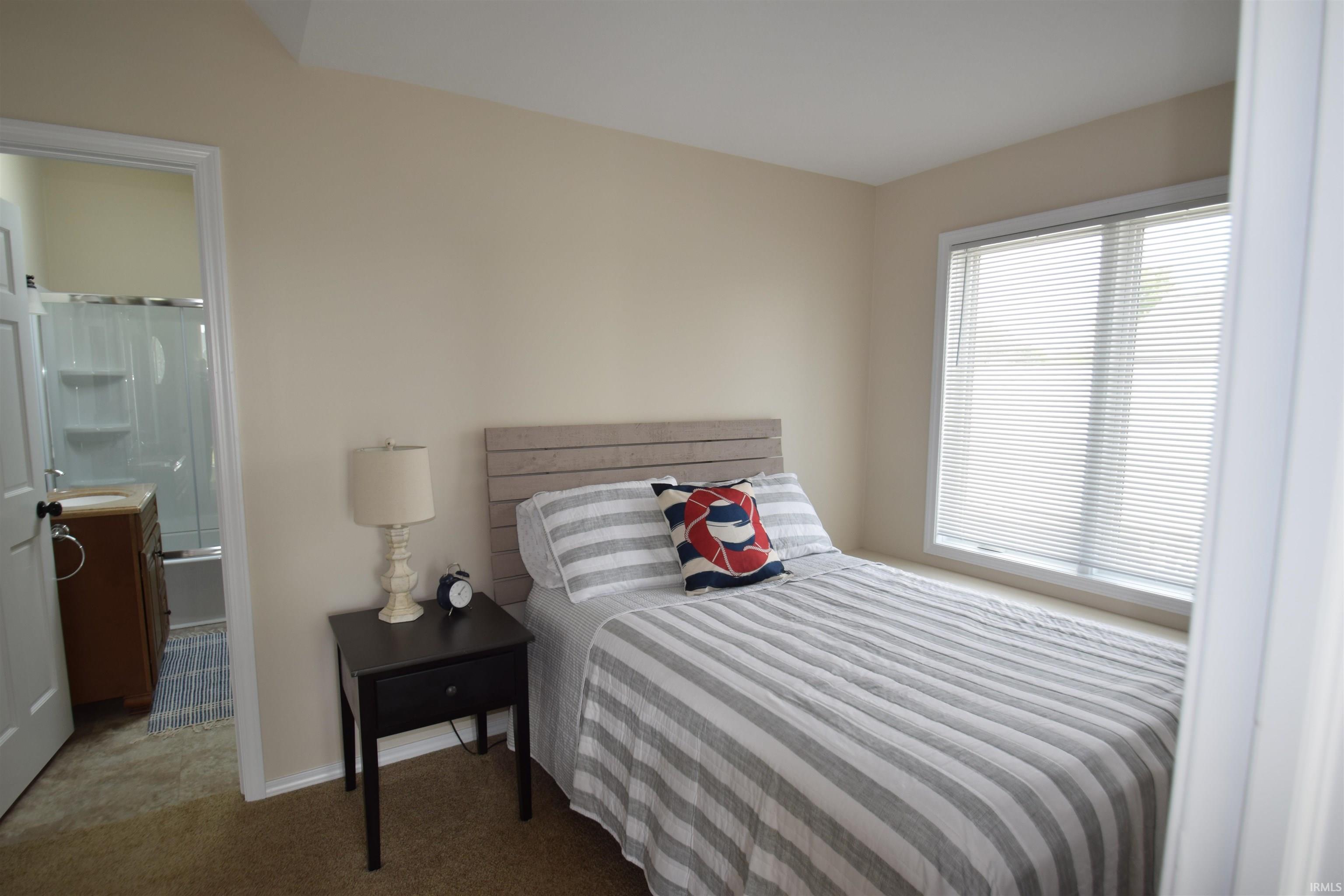 Carpeted bedroom featuring a large window with blinds and an attached full bathroom with a shower-over-tub