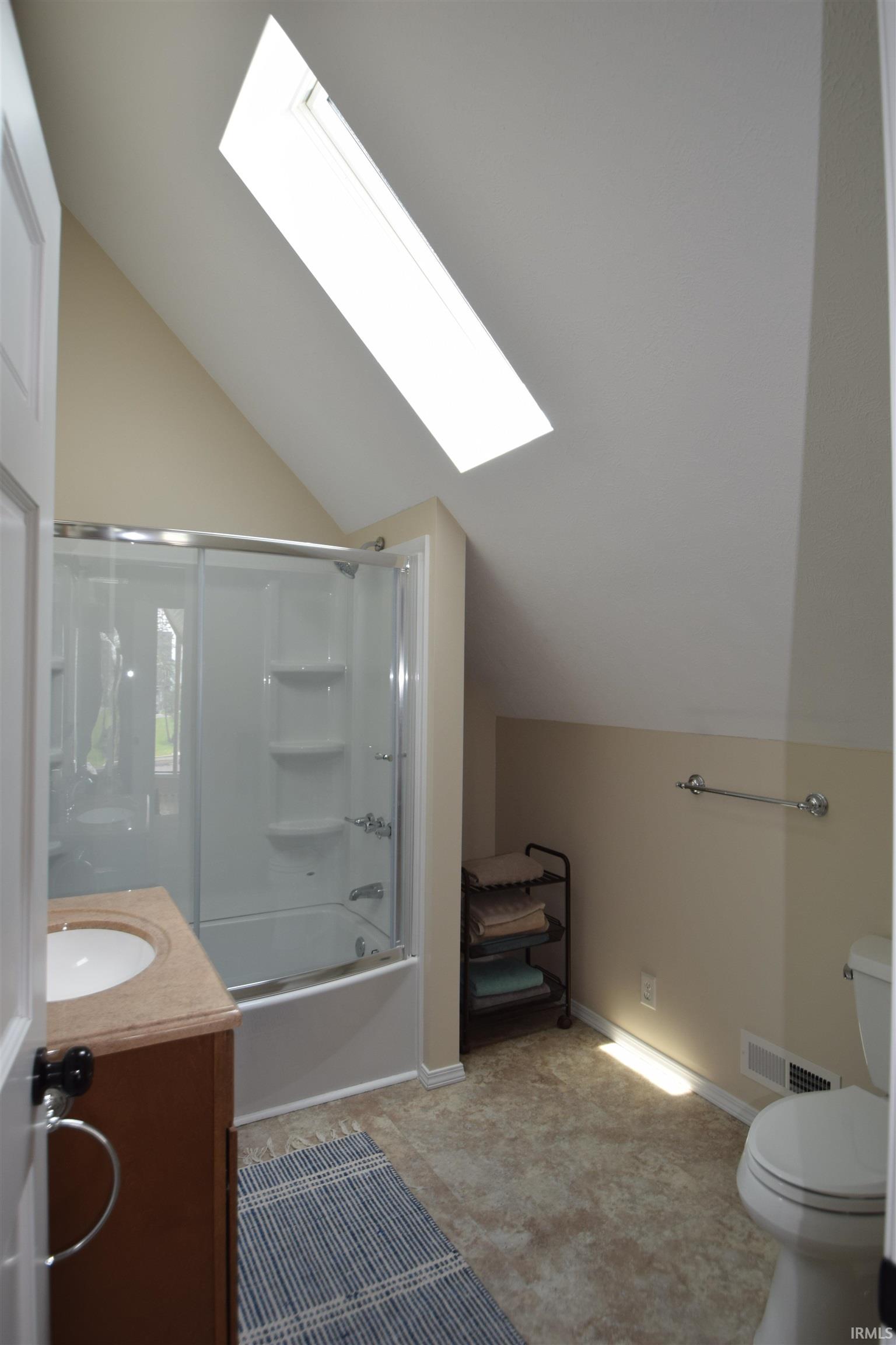 Bathroom featuring a skylight, a full shower/tub combination with sliding glass doors, a vanity with an integrated sink and wood-finish cabinetry, and a toilet