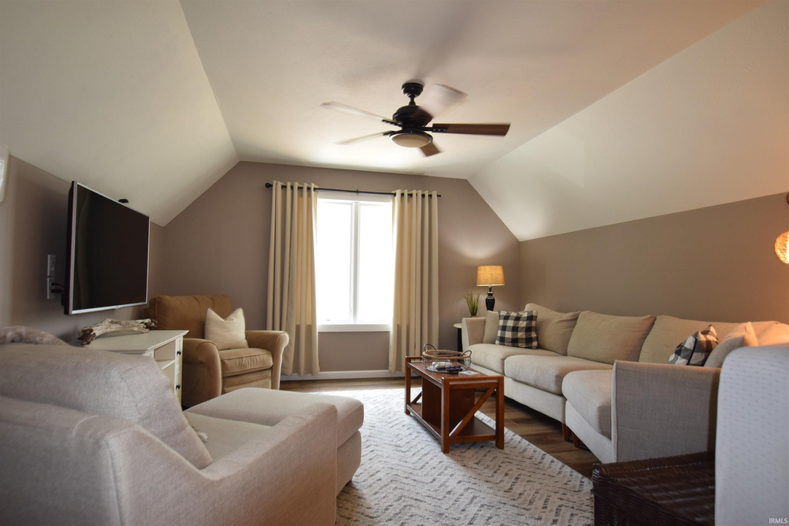 Spacious living area featuring sloped ceilings, a ceiling fan, and wood-finish flooring