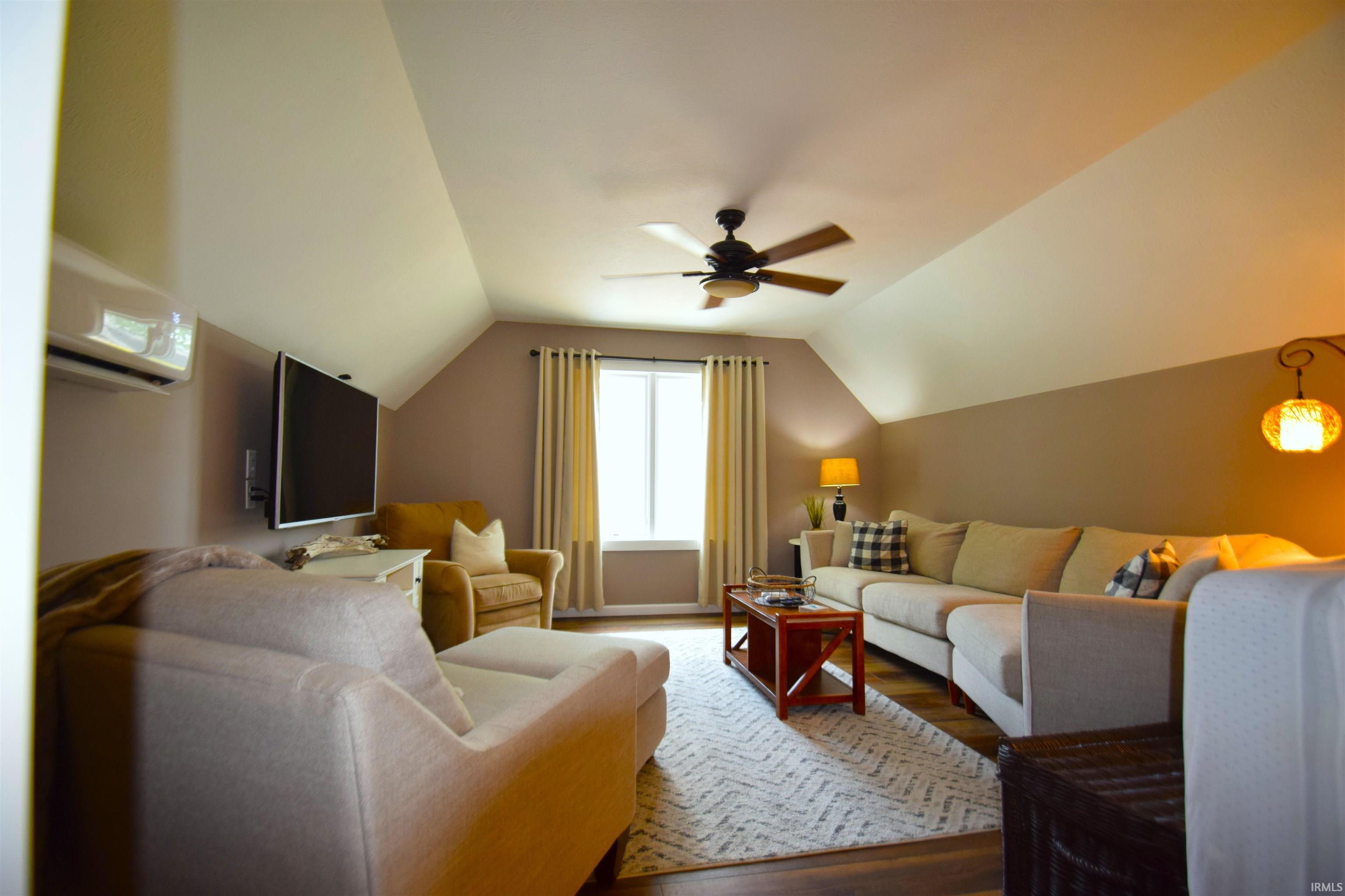 Attic living space featuring wood-finish flooring, a ceiling fan, and a wall-mounted television