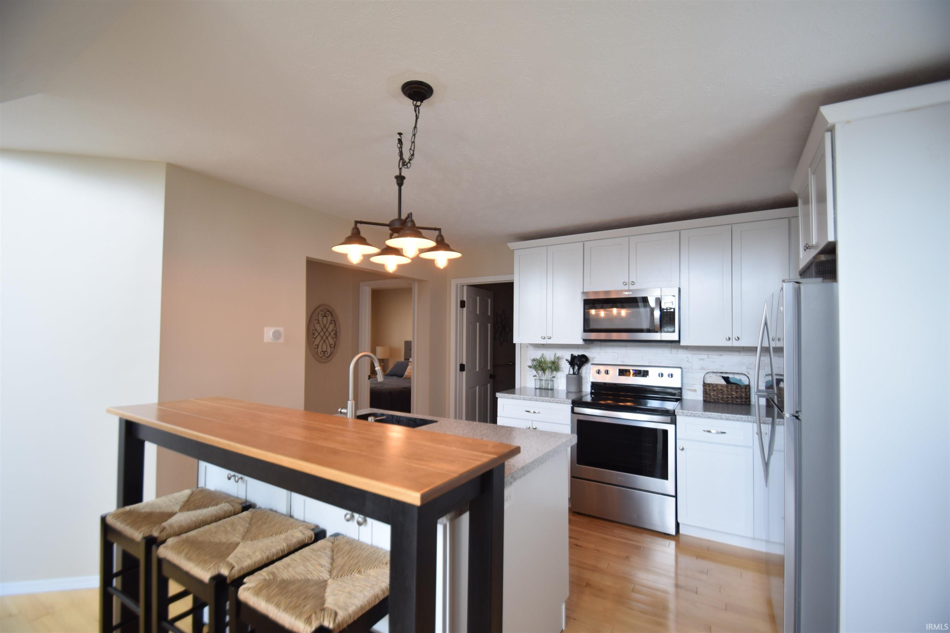 Kitchen featuring a large island with a wood-finish countertop, white cabinetry, stainless steel appliances, and wood-finish flooring