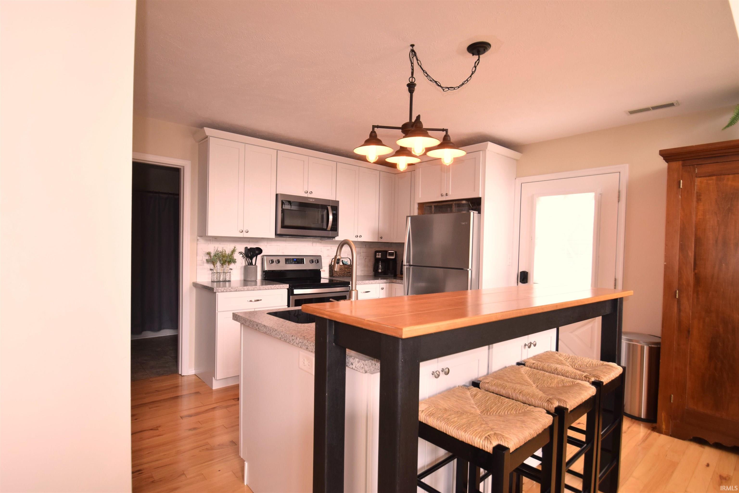 Kitchen featuring white cabinetry, stainless steel appliances, speckled countertops, and wood-finish flooring