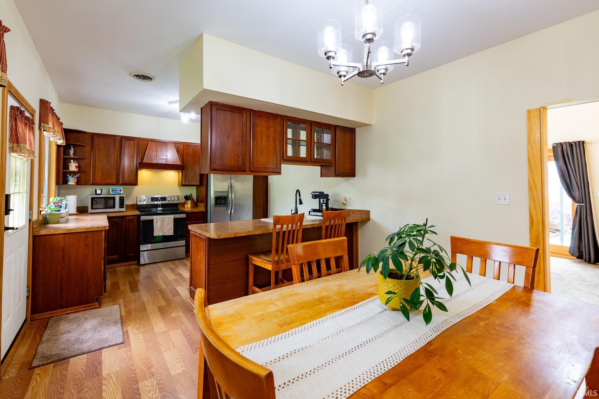 Open-concept kitchen and dining area featuring wood-finish flooring, abundant wood cabinetry, stainless steel appliances, and a breakfast bar with seating