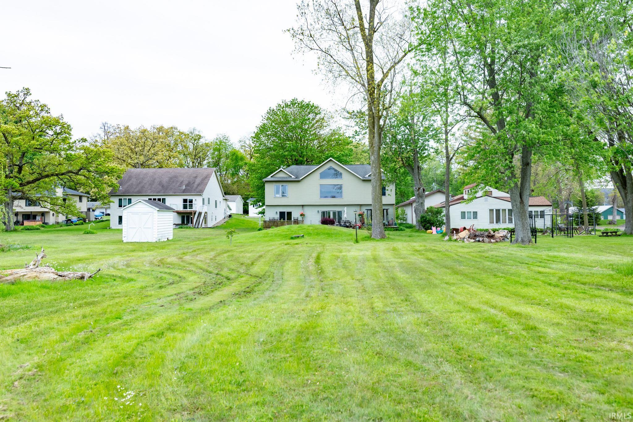 Expansive green lawn with mature trees and a white storage shed