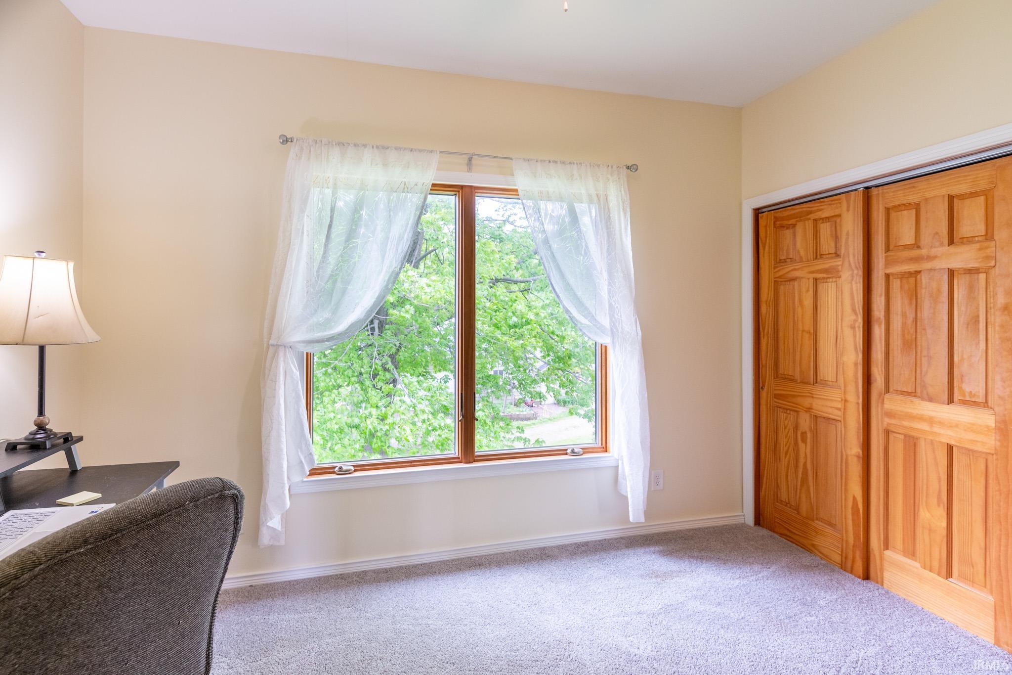 Room featuring light-toned wall paint, a large window with wood trim, and light gray carpeting