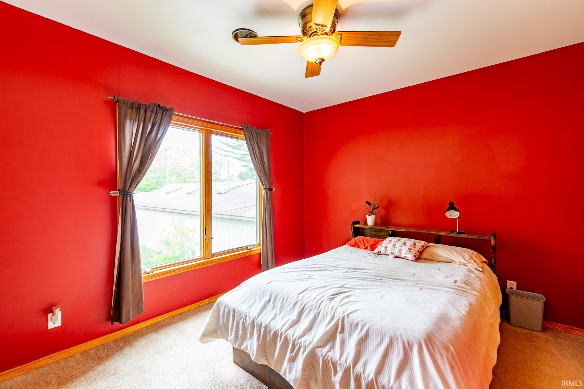 Brightly lit room featuring a large window with wood trim, a ceiling fan with integrated lighting, and carpet flooring