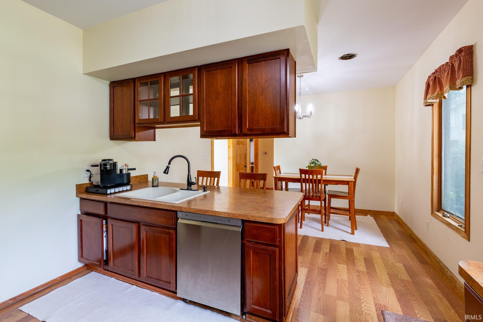Kitchenette area featuring wood-finish cabinetry, a stainless steel dishwasher, and a double basin sink with a matte black faucet