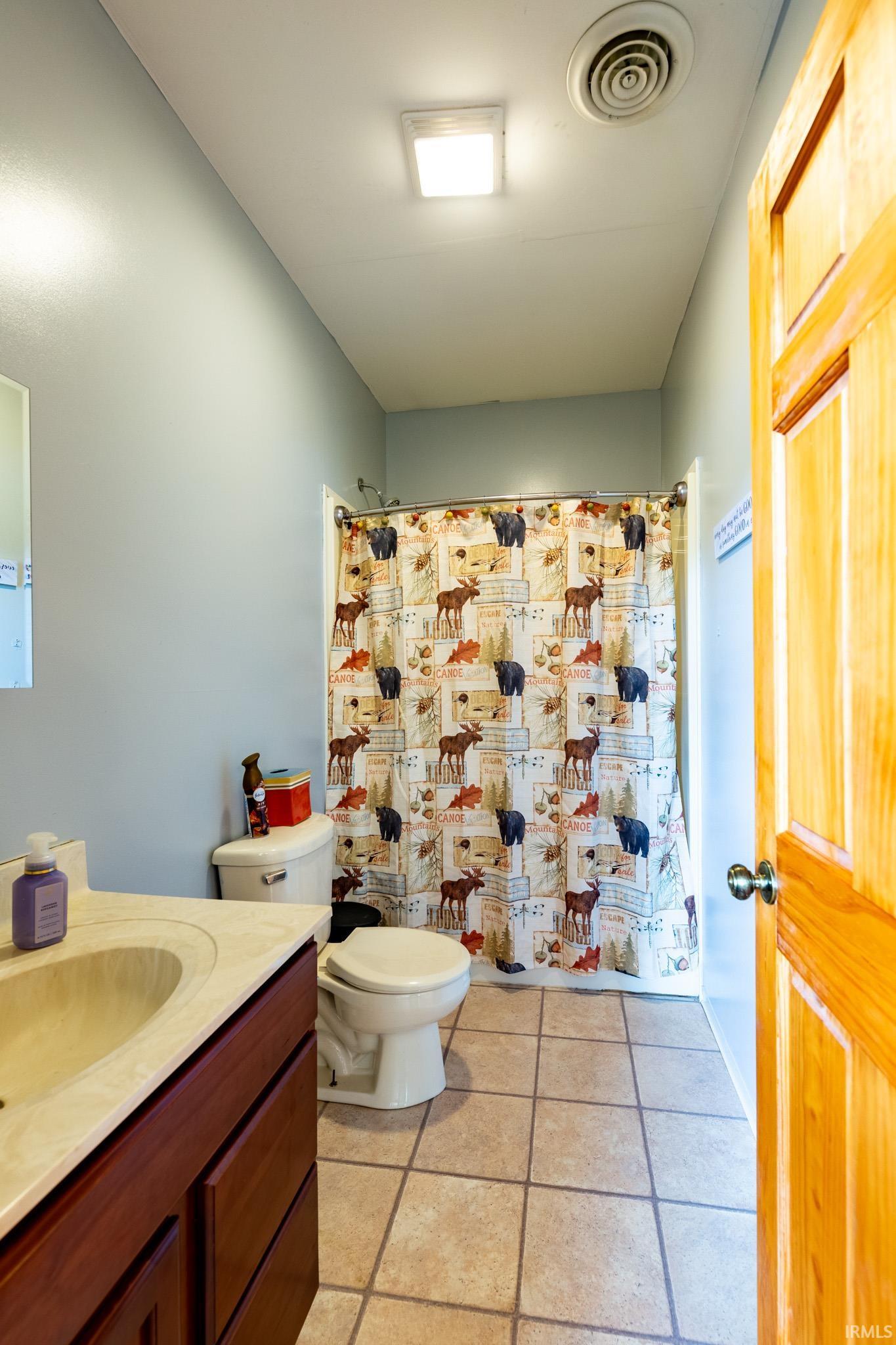 Bathroom featuring a wood-finish vanity with an integrated sink and light-toned countertop, a toilet, and a shower area with a curtain
