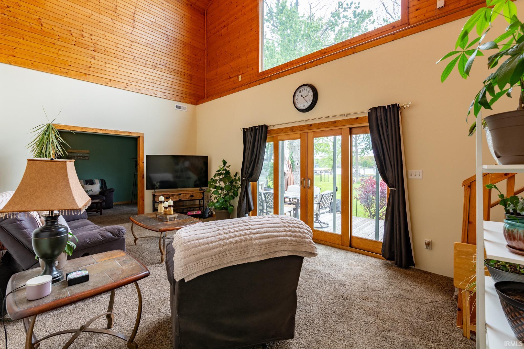 Vaulted wood-paneled ceiling with clerestory windows, large sliding glass doors providing access to an exterior deck, wall-mounted television console, and recessed lighting