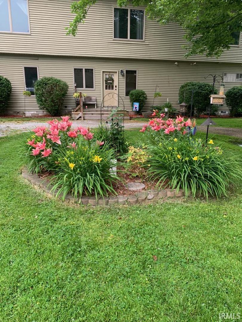 Landscaped front yard featuring a curved stone-edged garden bed with mature flowering plants