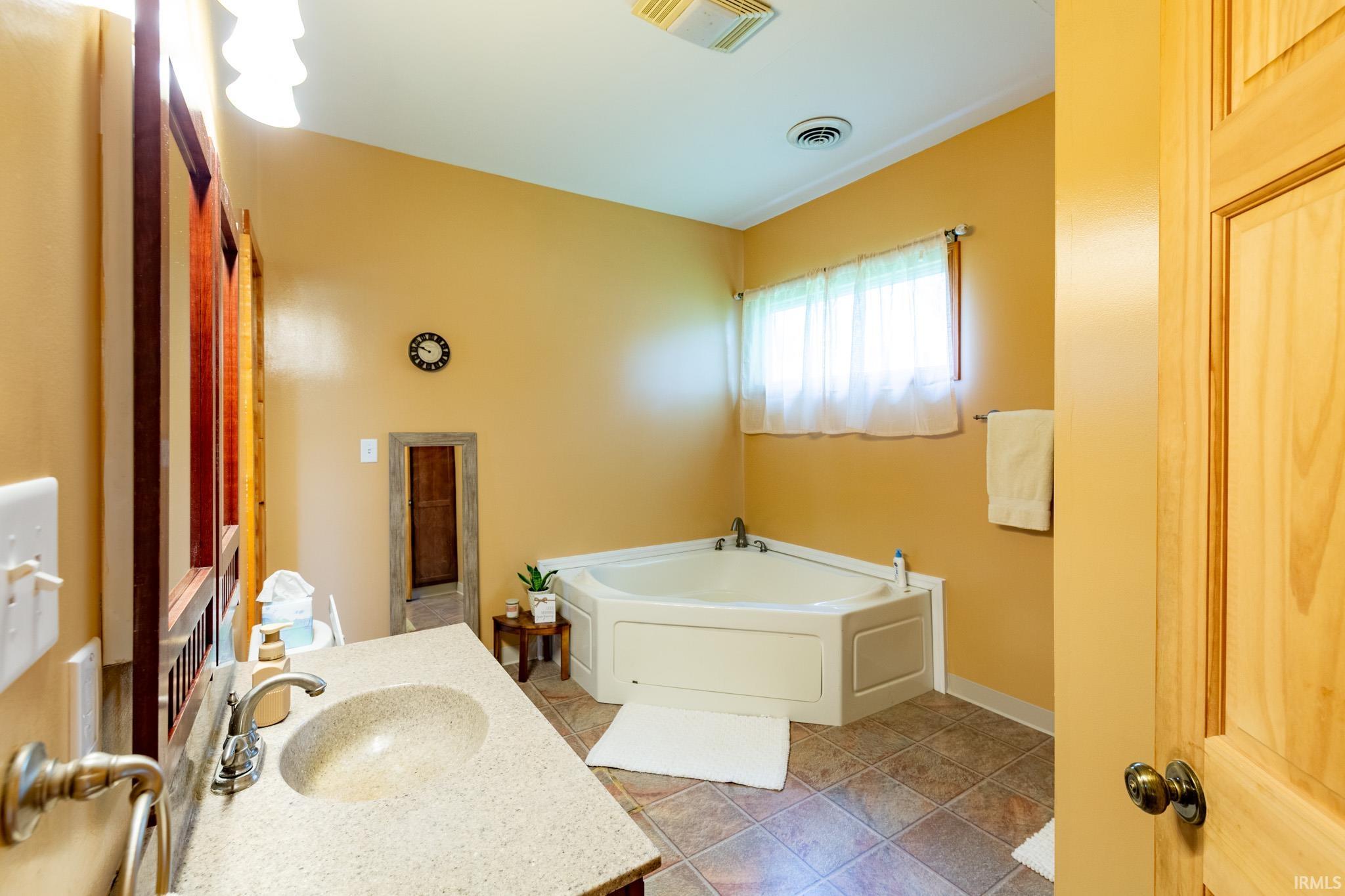 Bathroom featuring a corner soaking tub, a single vanity with a stone-finish countertop, and tile flooring