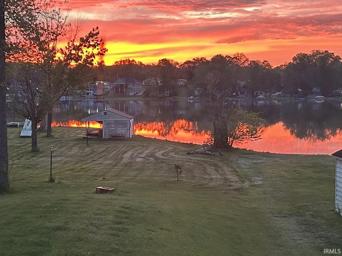 Waterfront property featuring a boathouse, mature trees, and a spacious lawn