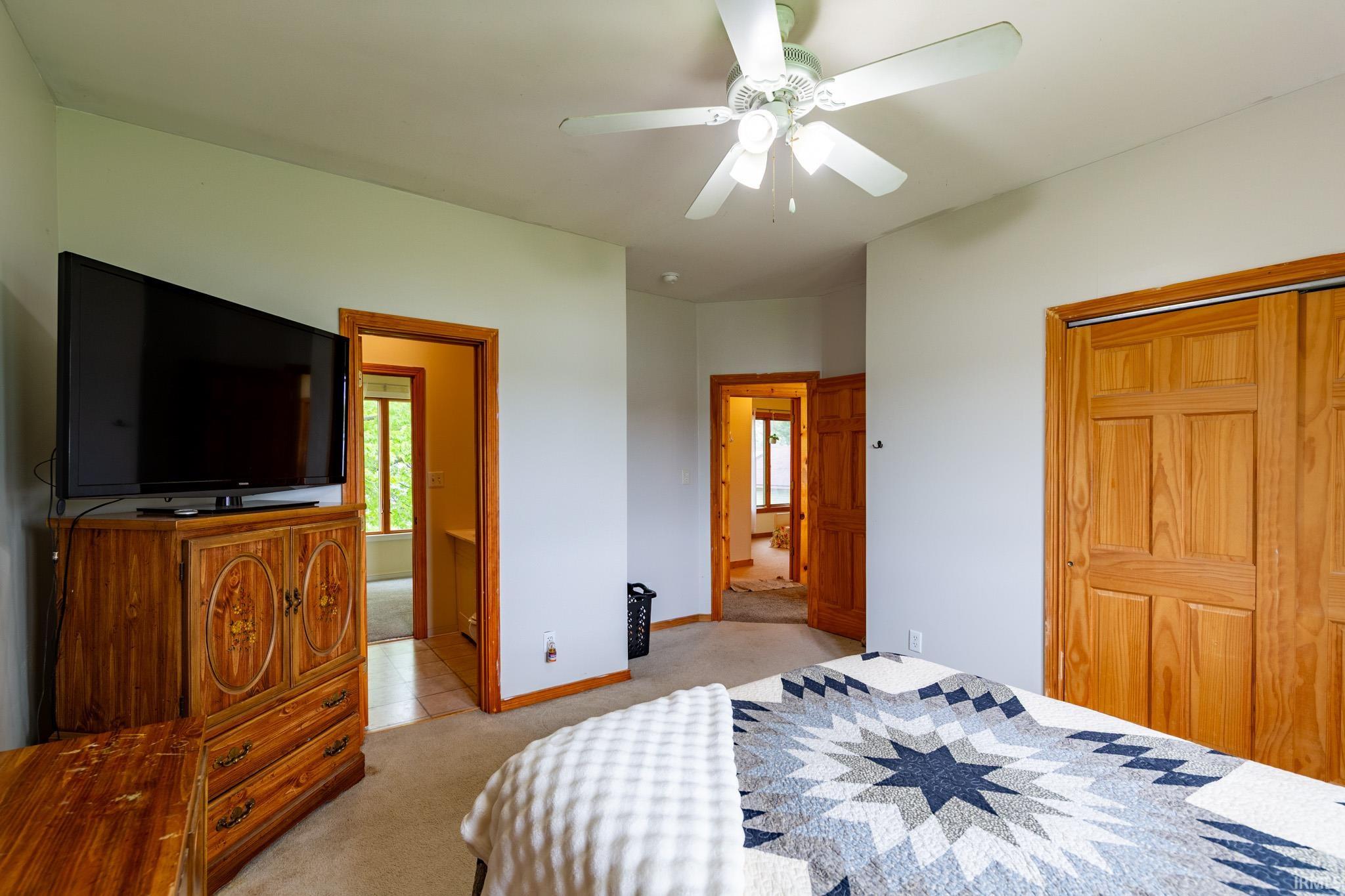 Carpeted interior space featuring a ceiling fan with integrated lighting, natural wood-finish trim, and multiple paneled doors