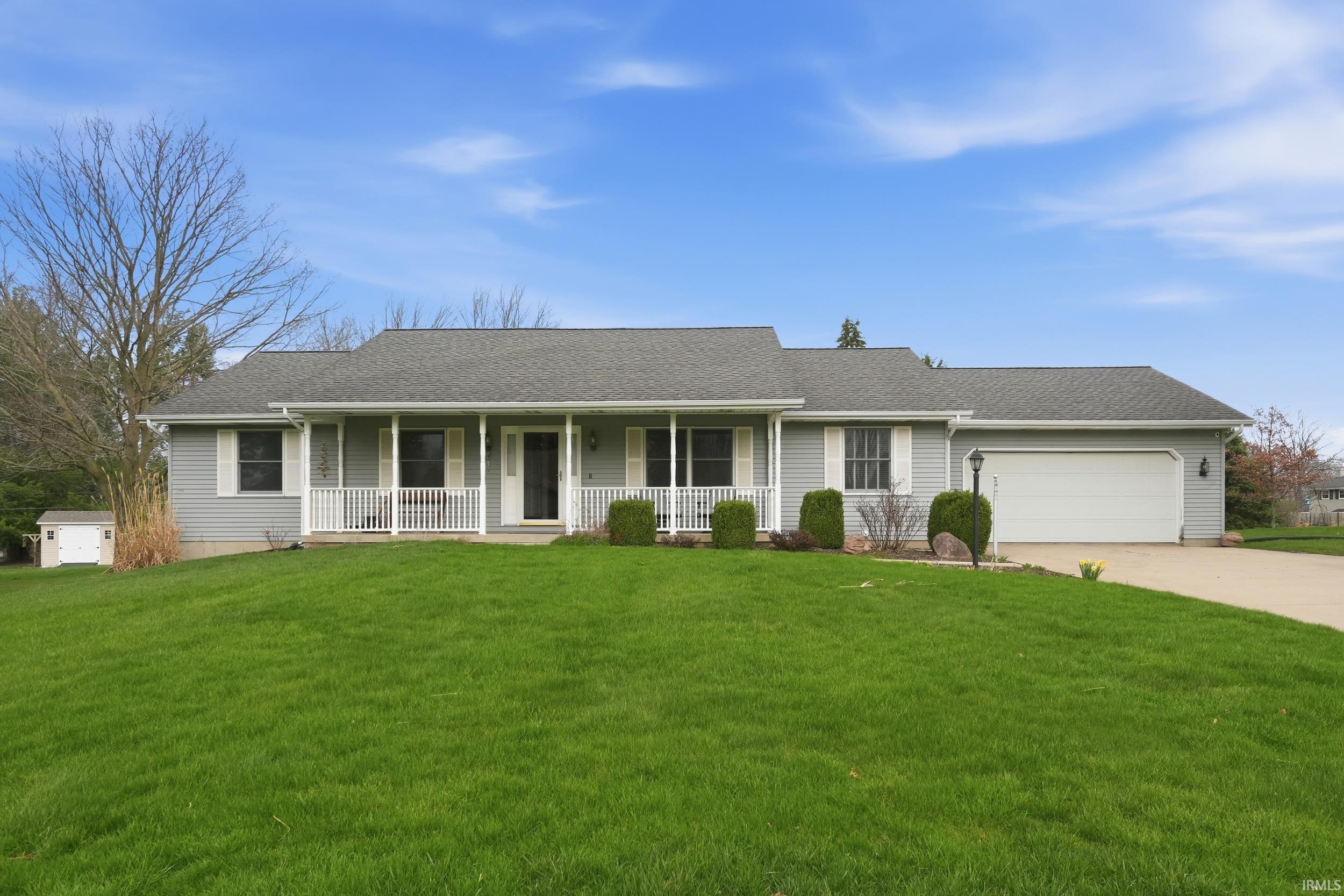 Ranch-style home with a shingled roof, a porch, a front yard, and an attached garage