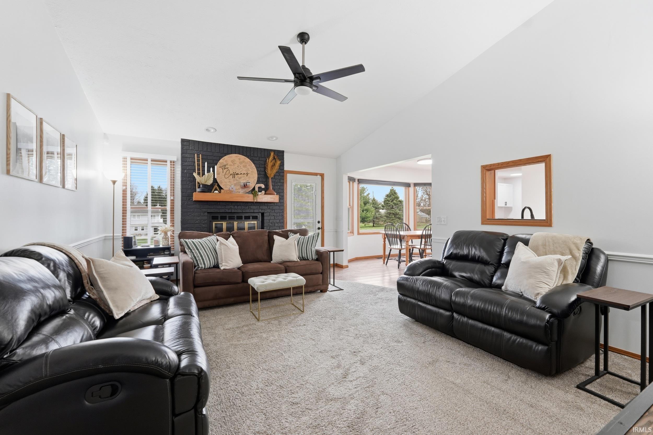 Living room featuring carpet, a ceiling fan, a fireplace, and vaulted ceiling