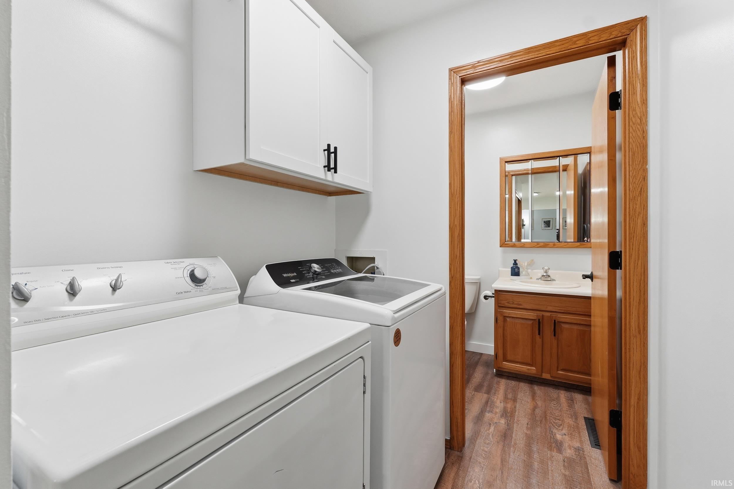 Laundry area featuring dark wood-style flooring, cabinet space, and washer and clothes dryer
