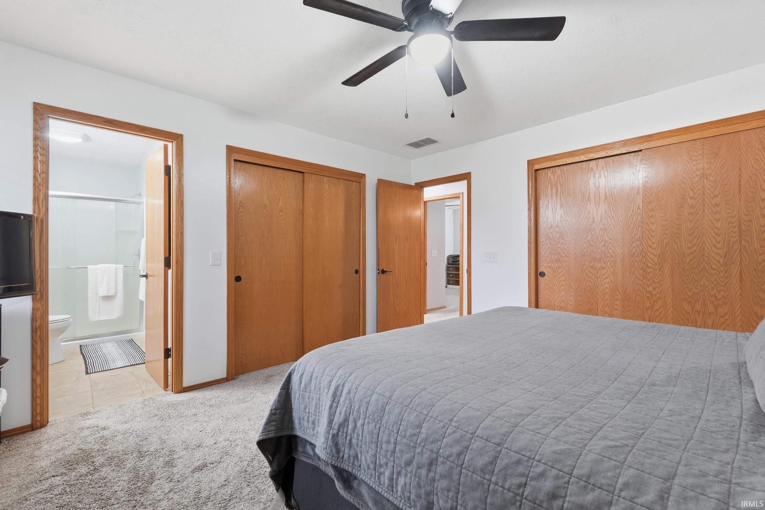 Bedroom with multiple closets, light carpet, connected bathroom, and a ceiling fan