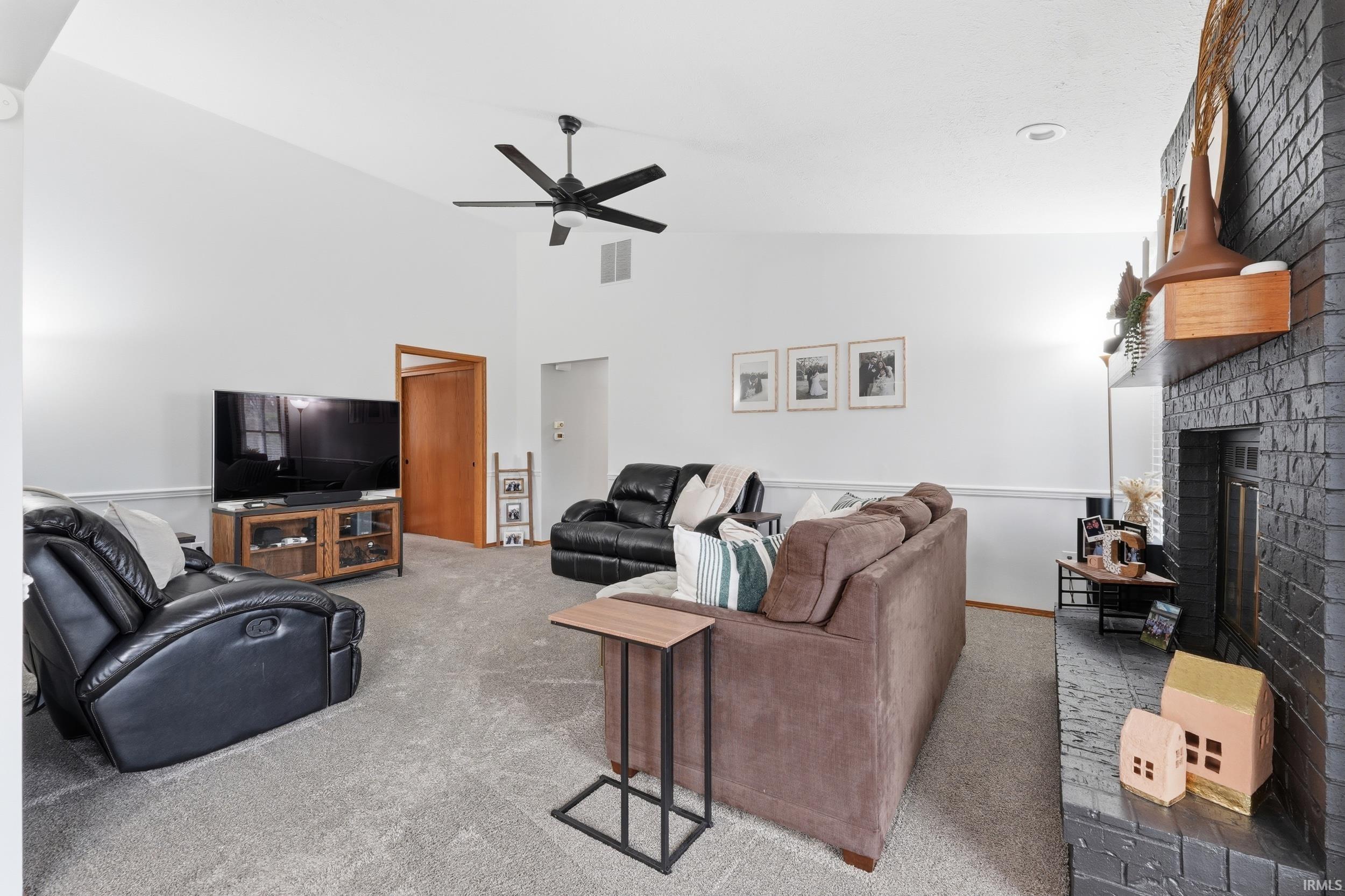 Carpeted living area with vaulted ceiling, a brick fireplace, and ceiling fan
