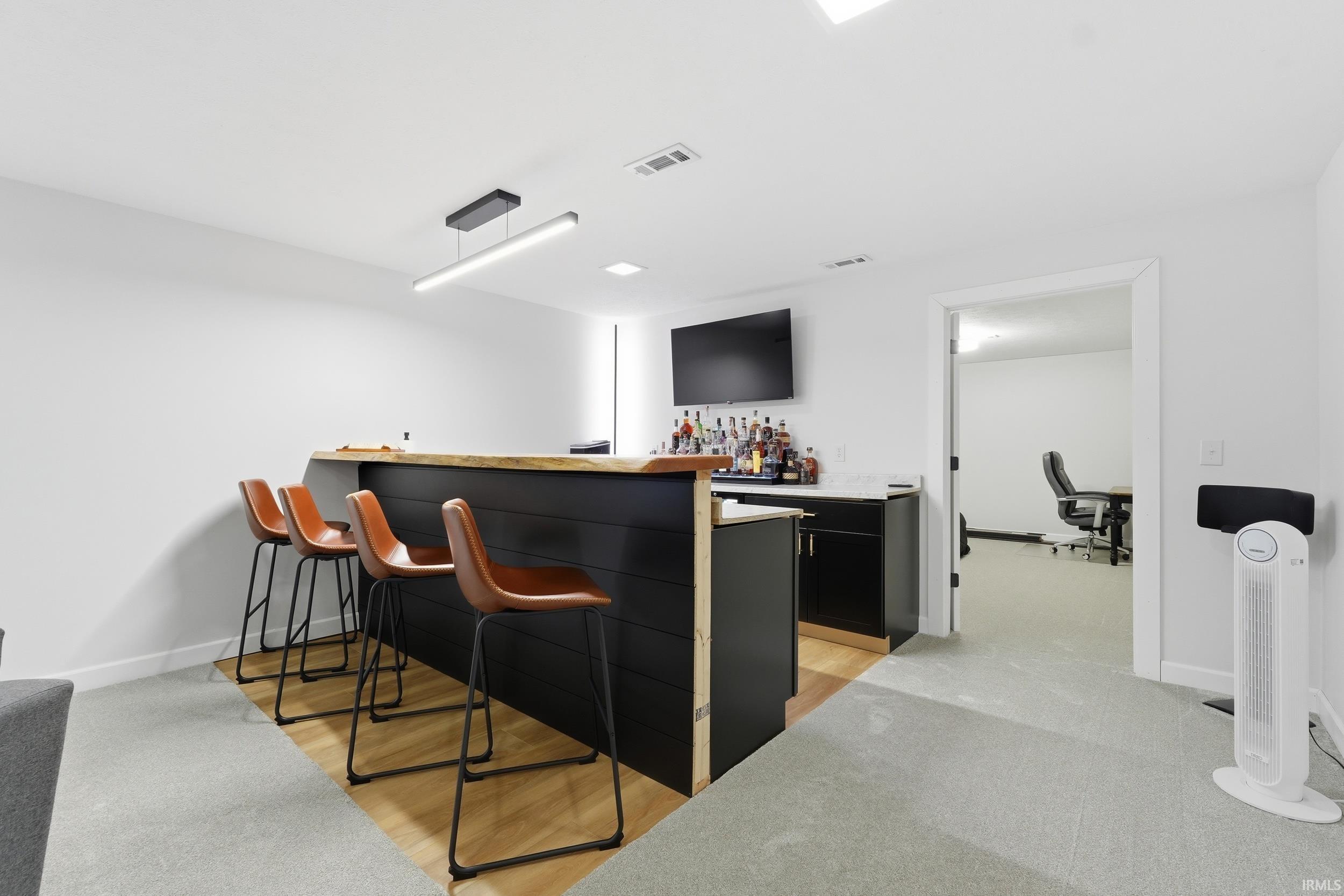 Indoor dry bar with dark cabinets and light wood-type flooring