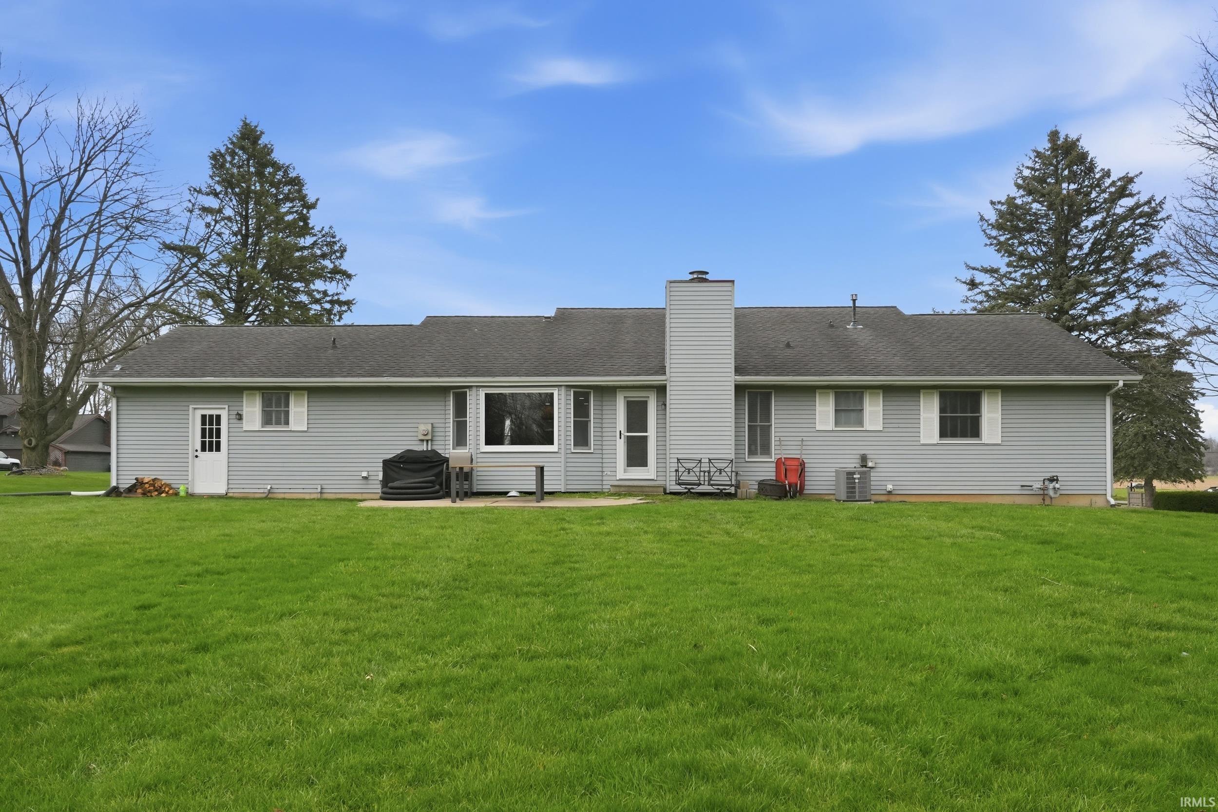 Back of house featuring a chimney, a yard, a patio, and roof with shingles