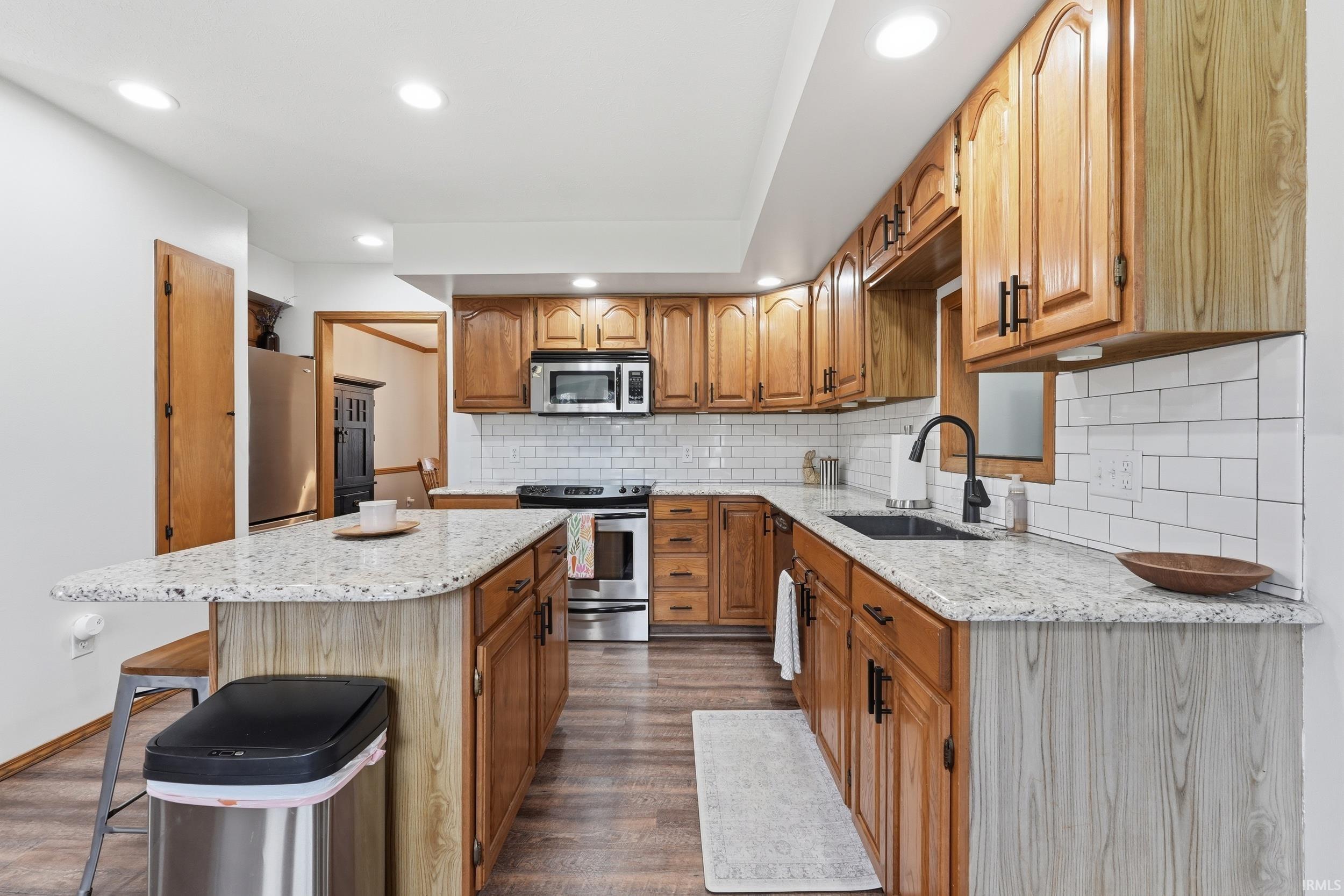 Kitchen with a kitchen island, a breakfast bar, stainless steel appliances, light stone counters, and recessed lighting