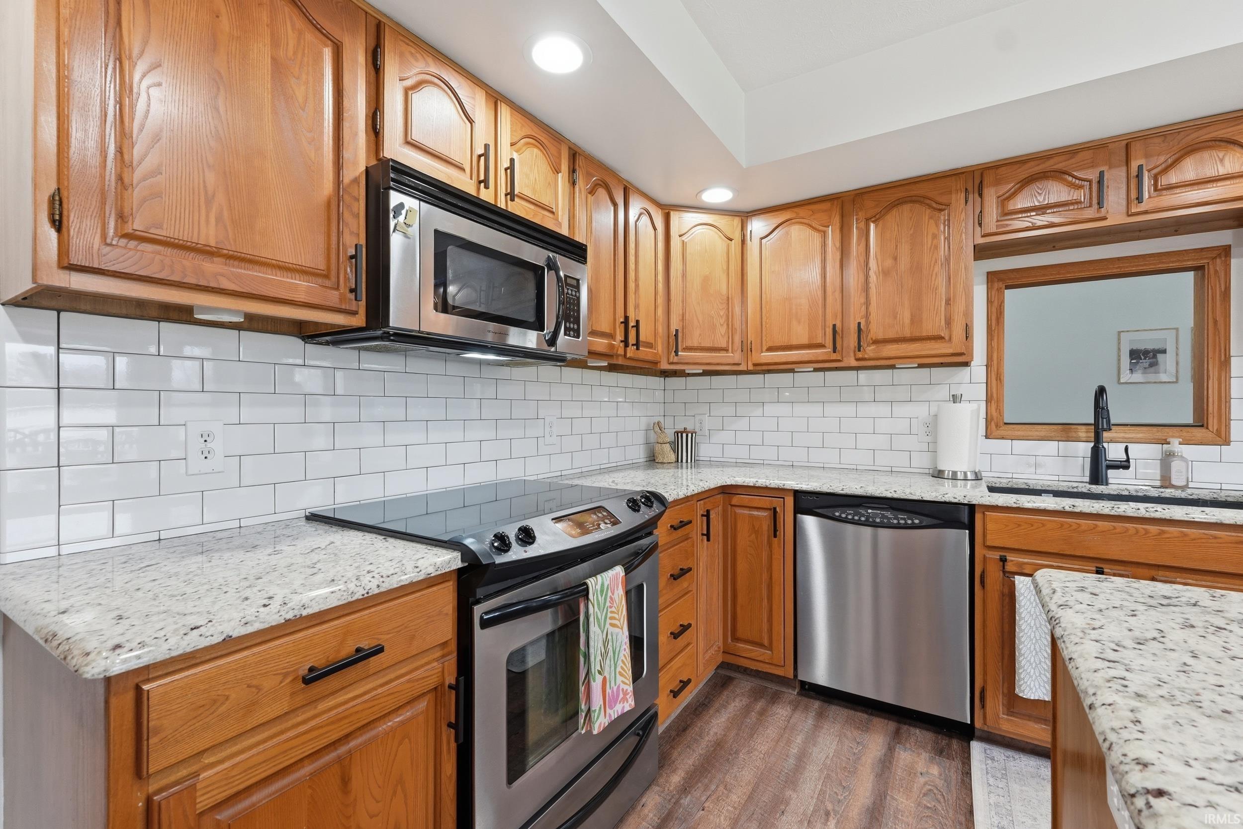Kitchen featuring stainless steel appliances, light stone countertops, wood finish cabinetry, and recessed lighting