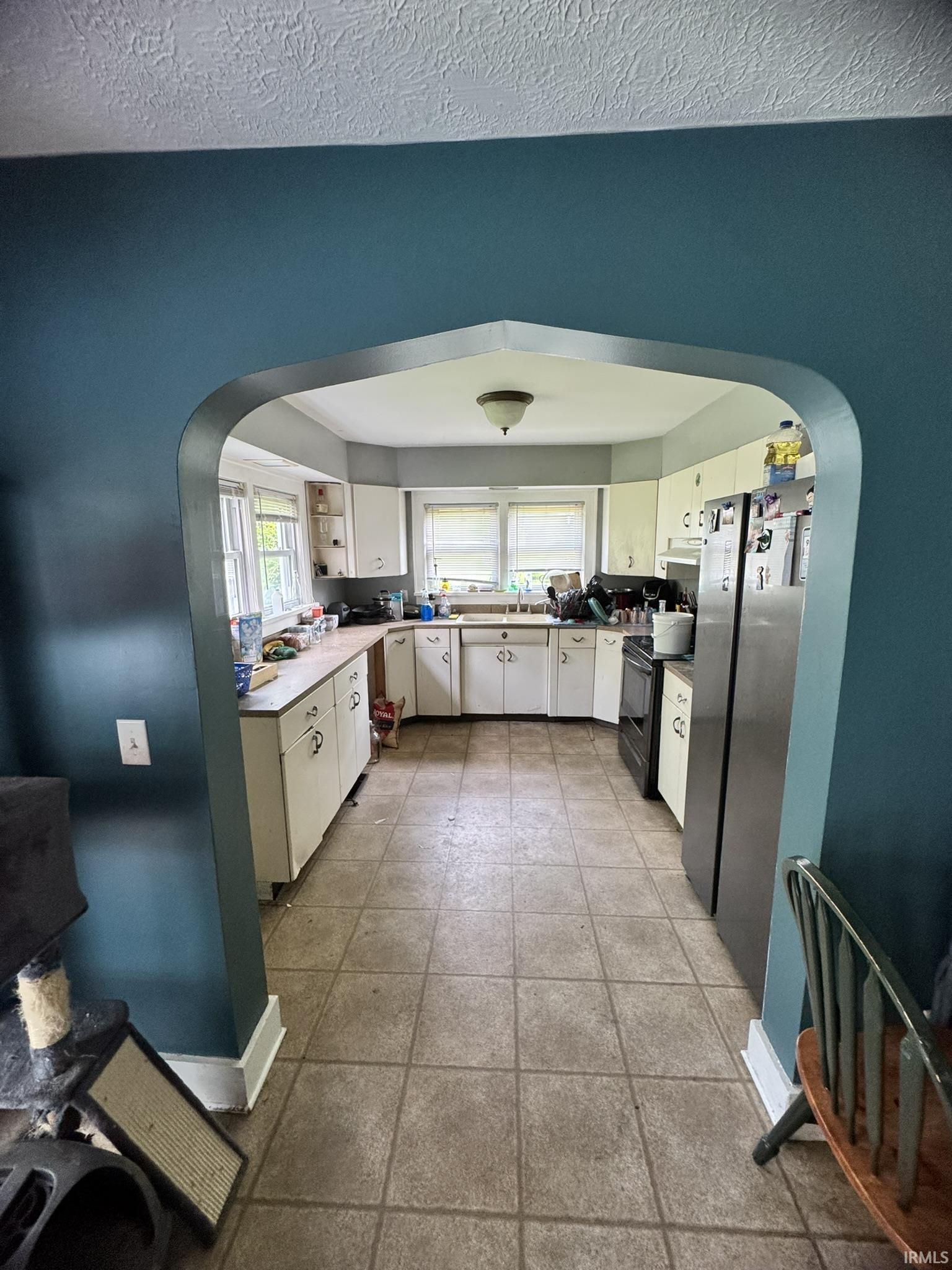 Kitchen featuring an arched entryway, tile flooring, white cabinetry, and stainless steel appliances