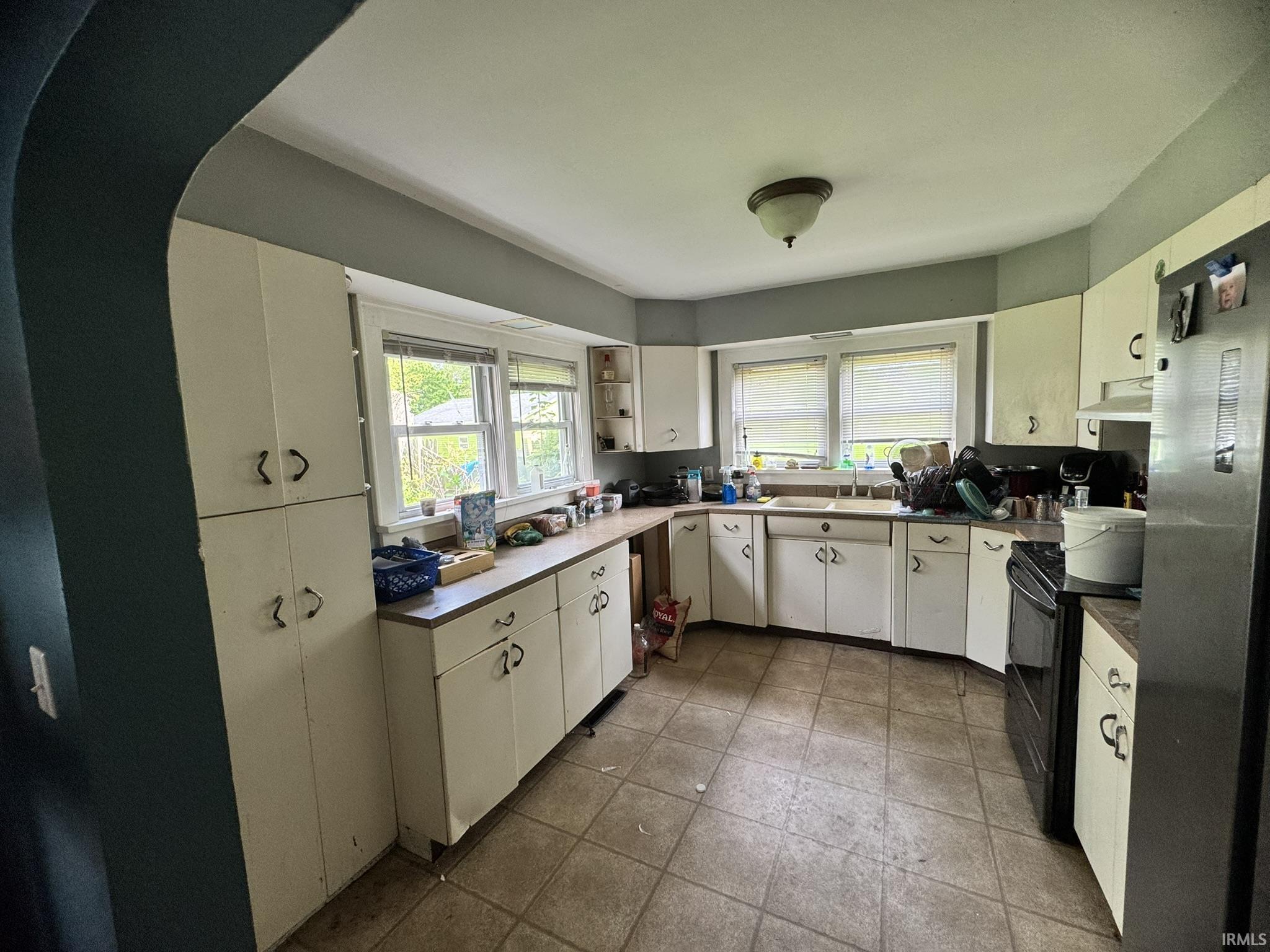 Spacious kitchen featuring extensive white cabinetry, durable tile flooring, multiple windows, a ceiling-mounted light fixture, and ample counter space