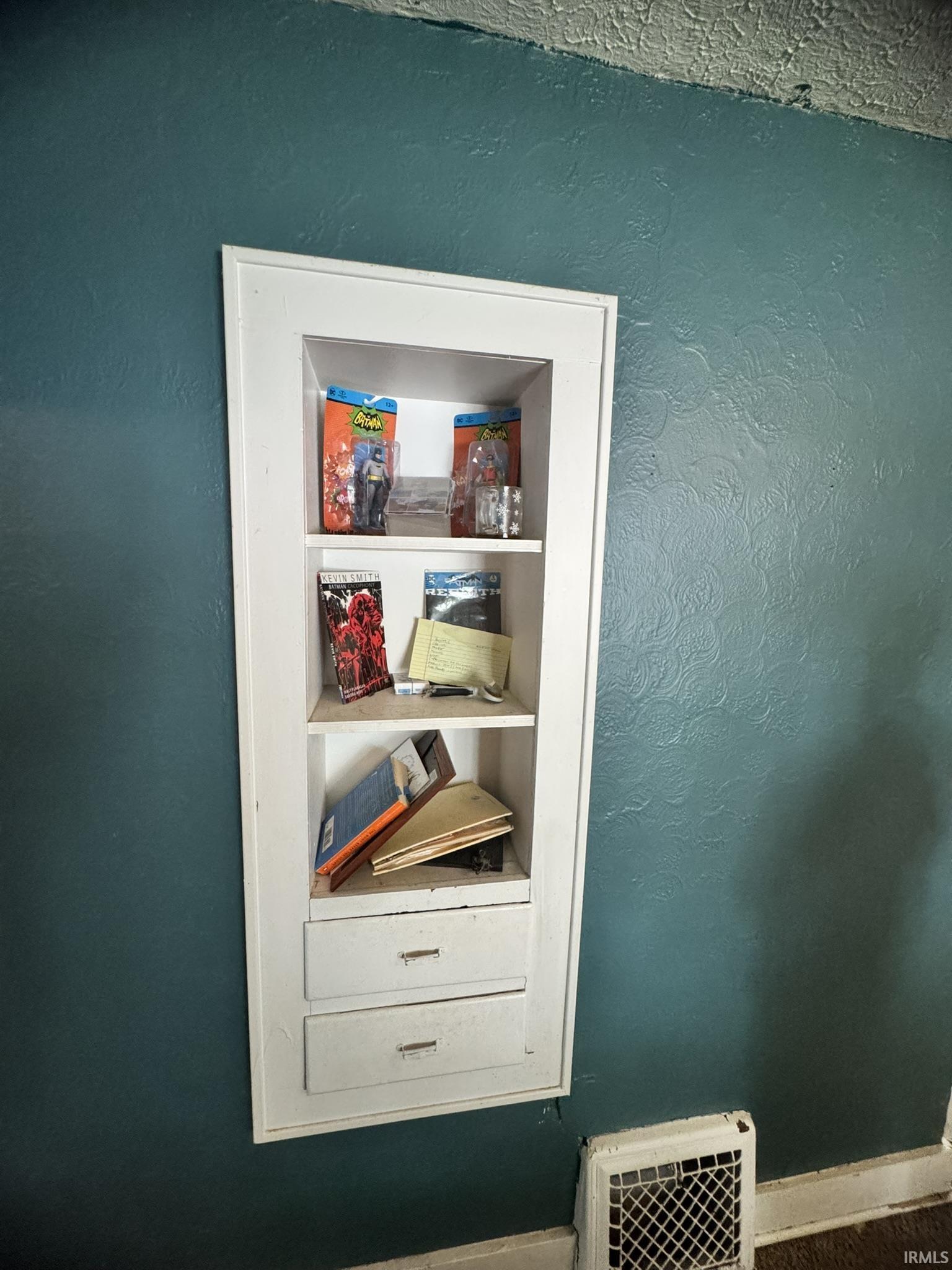 Built-in shelving unit featuring three open shelves and two lower storage drawers with metal pulls, set into a textured wall