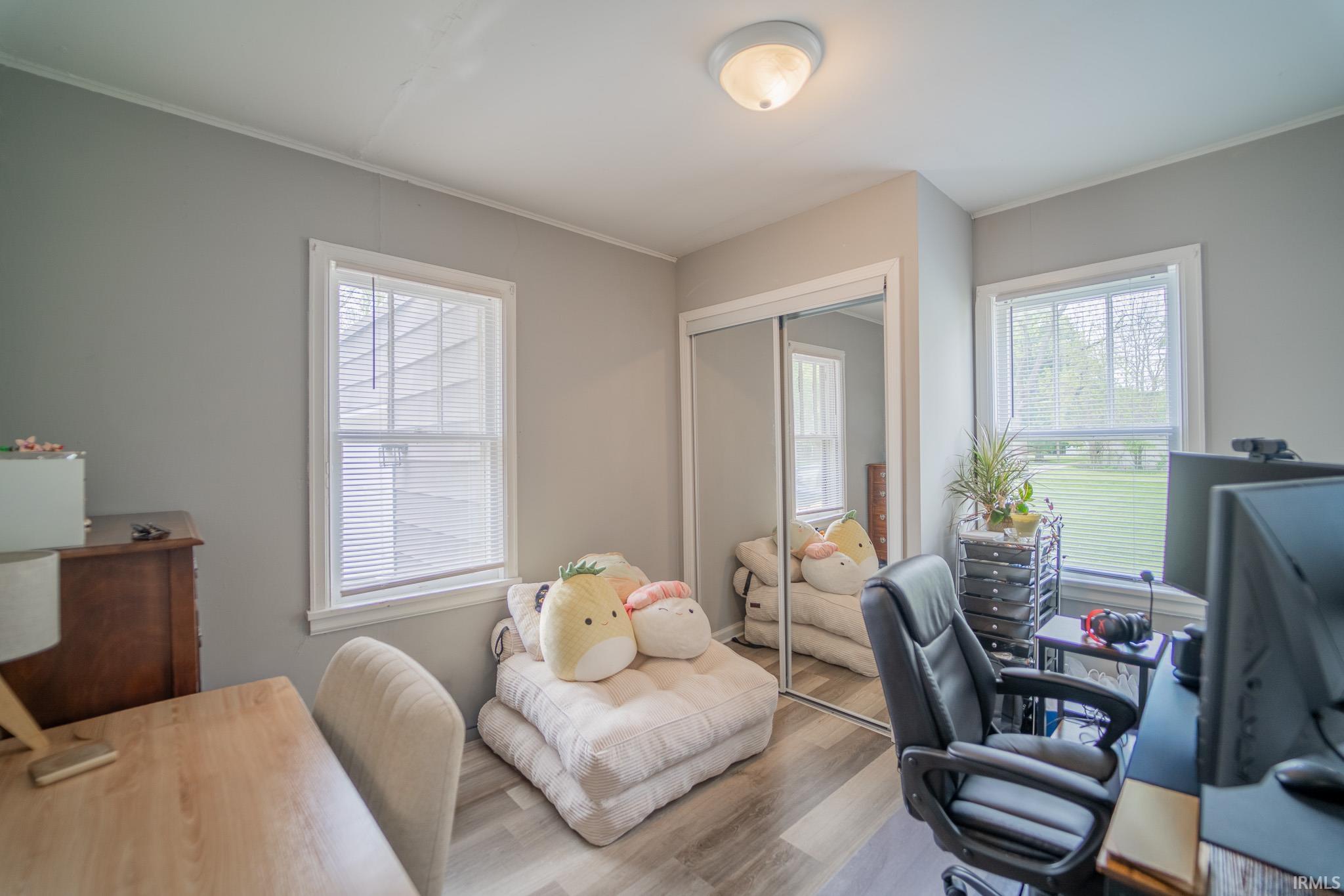 Laminate wood-finish flooring, two large windows with blinds, mirrored closet doors, recessed ceiling light fixture, and crown molding