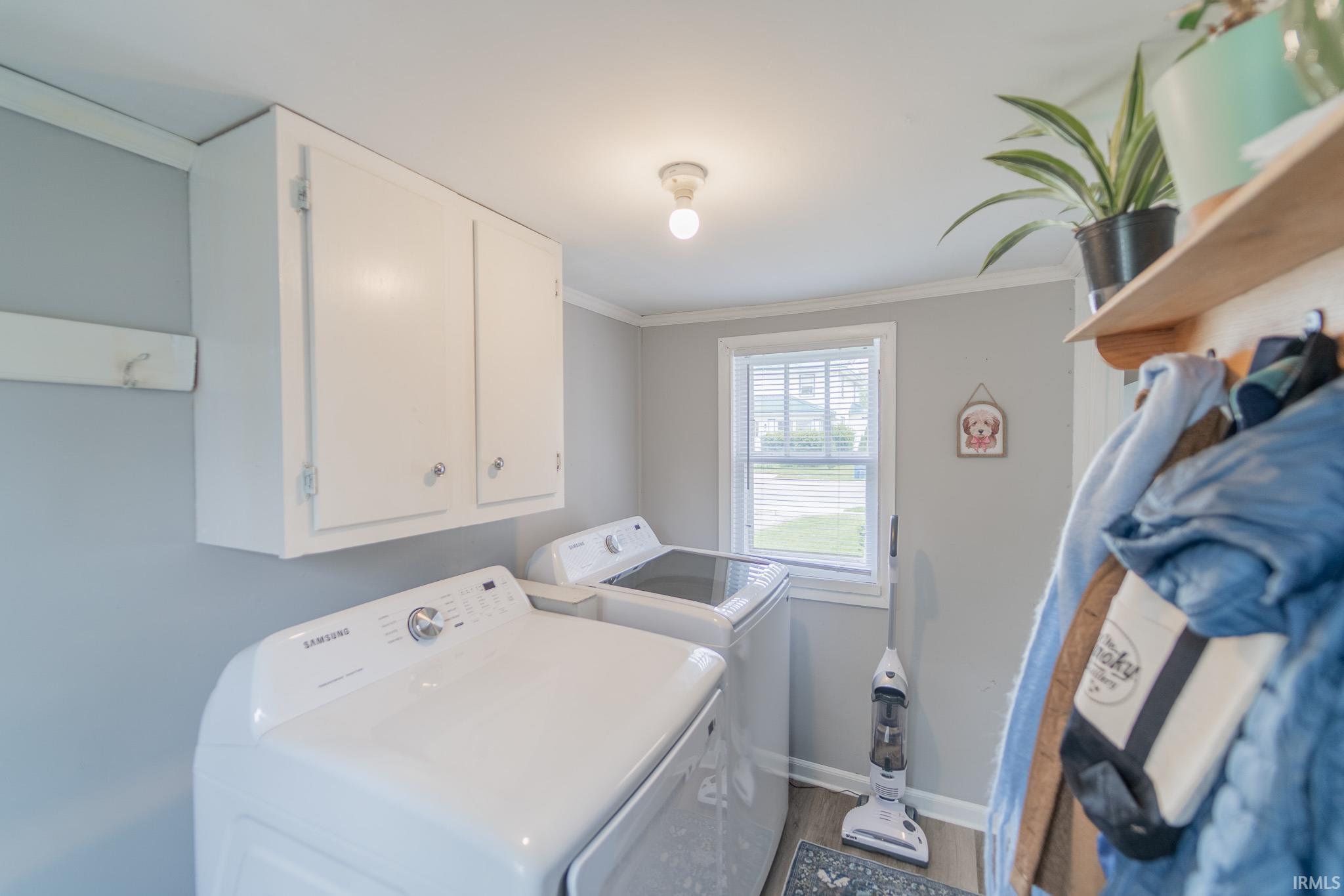 Laundry area featuring white cabinetry, a large window with blinds, and wood-finish flooring
