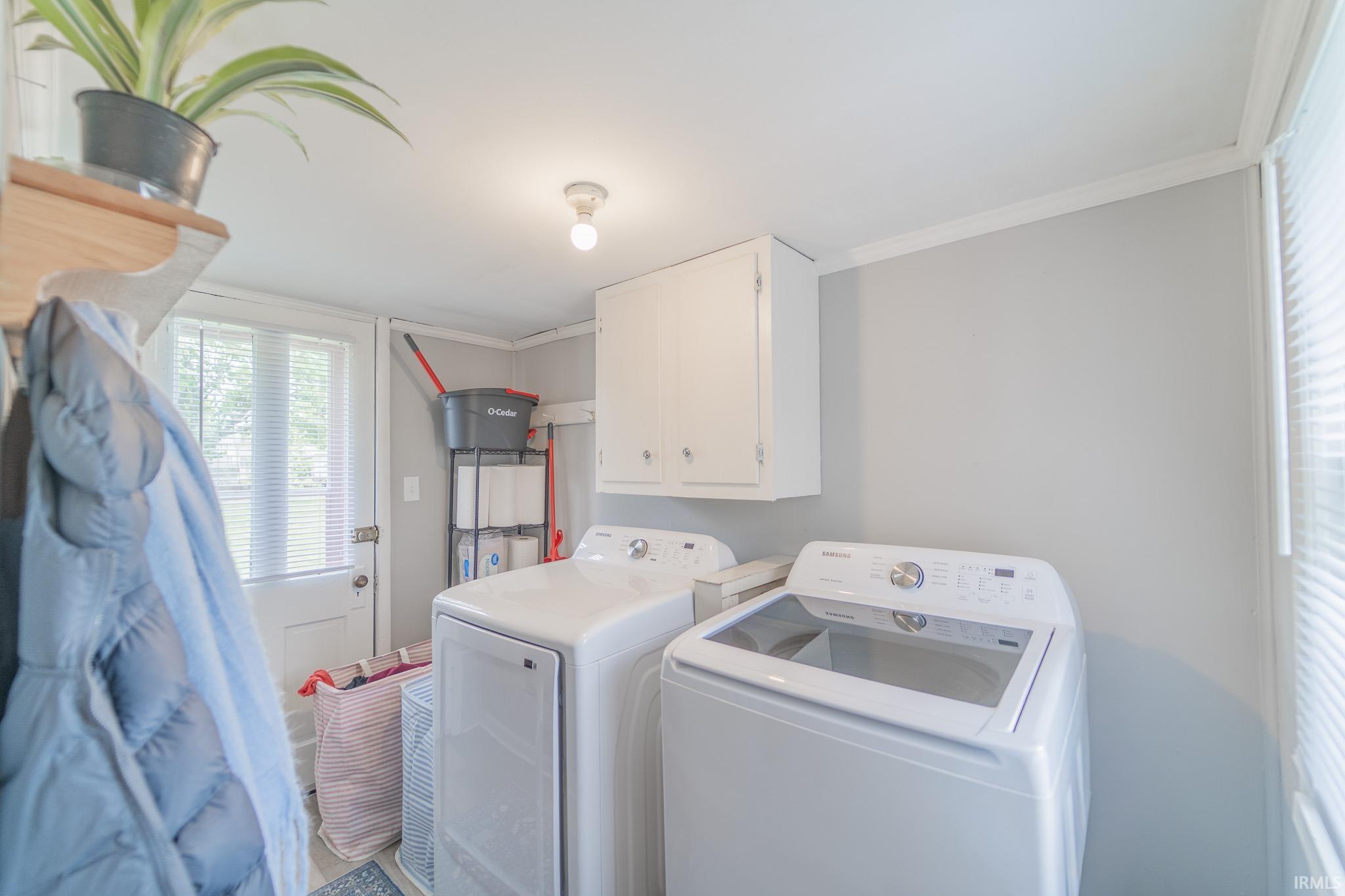 Dedicated laundry space featuring white appliances, upper cabinetry, and a window with blinds