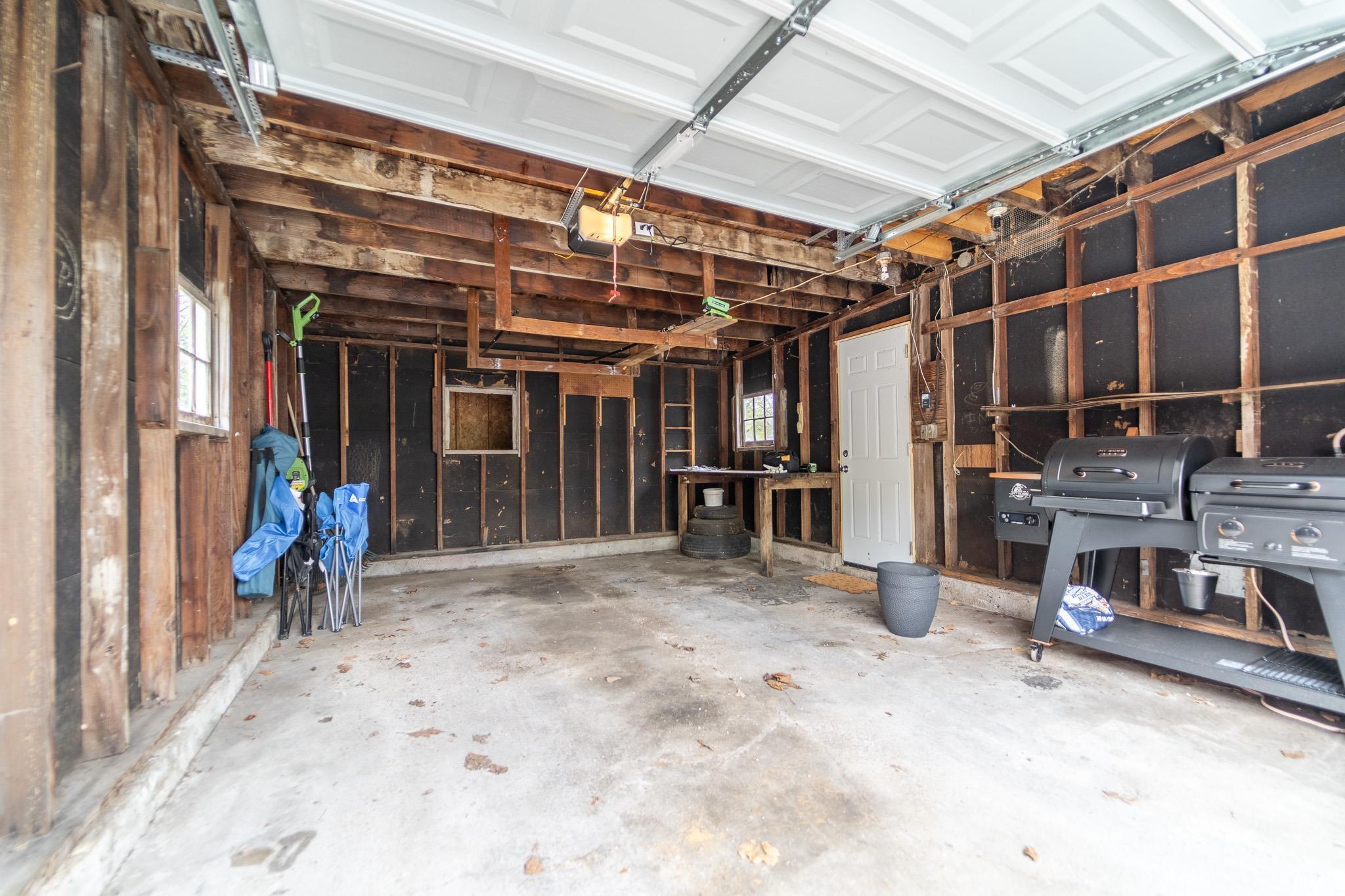 Spacious garage interior featuring an overhead white panel garage door, exposed wood framing, and a concrete floor
