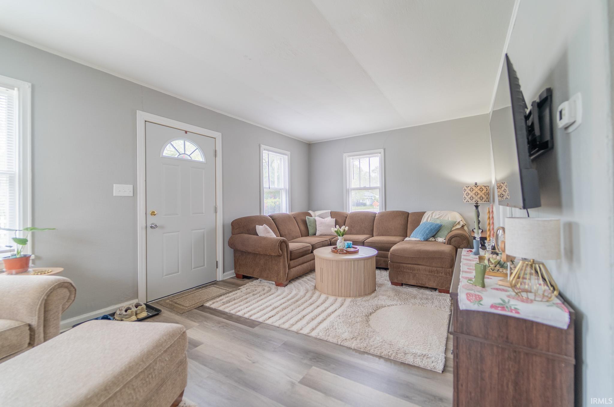 Living area featuring light gray wall paint, wood-finish flooring, multiple windows, and a front entry door with an arched window insert