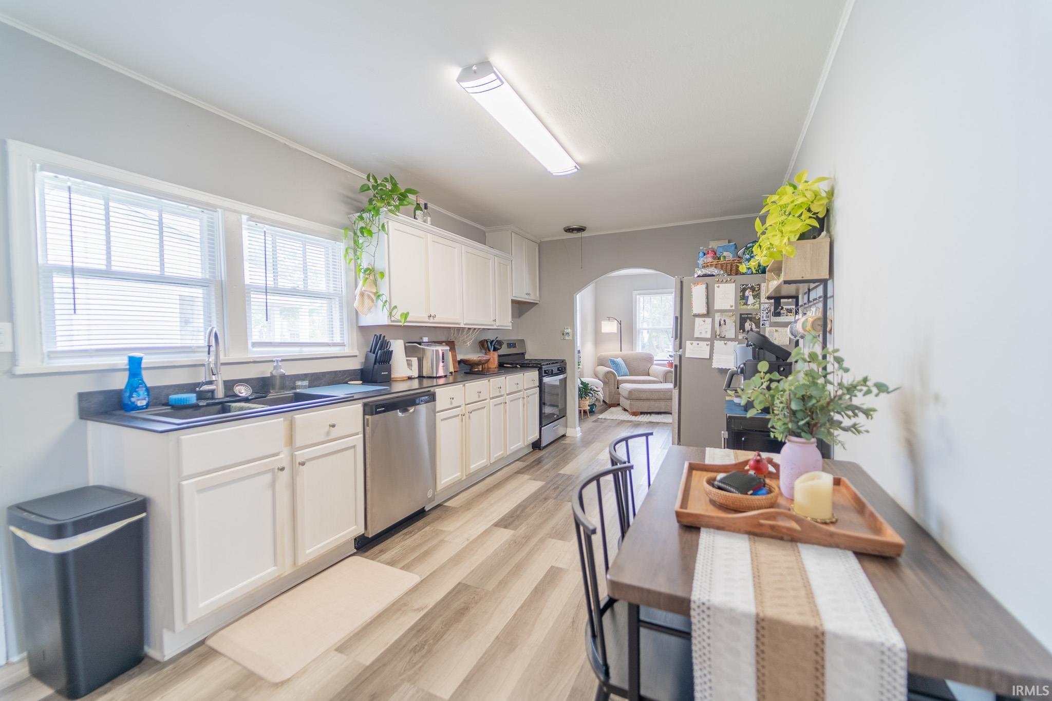 Kitchen featuring white cabinetry, dark countertops, wood-finish flooring, stainless steel dishwasher, and dual windows above the sink
